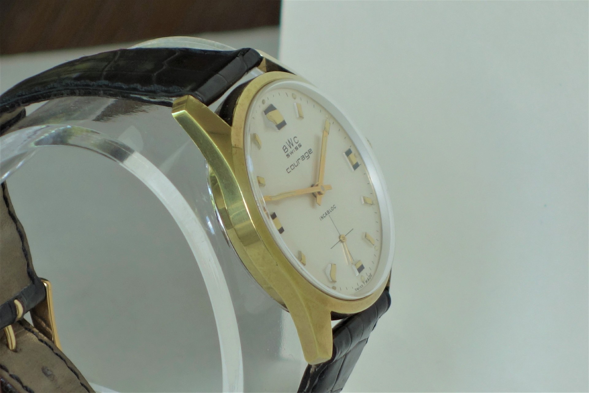 Analoge Armbanduhr mit goldfarbenem Gehäuse, hellem Zifferblatt und schwarzem Lederarmband.