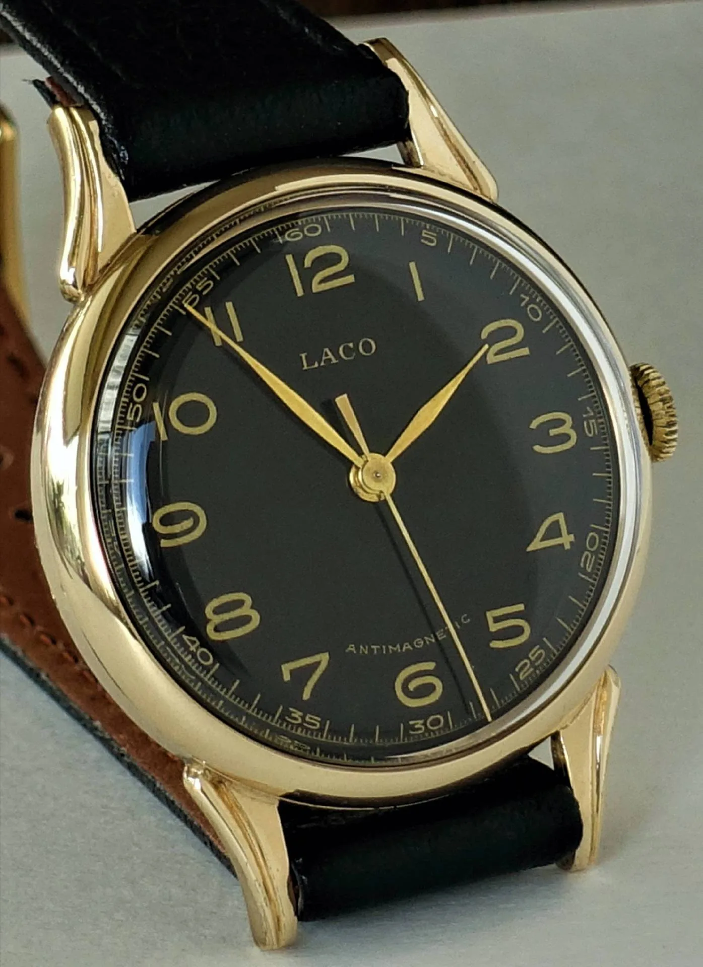 Analoge Armbanduhr mit schwarzem Zifferblatt, goldfarbenem Gehäuse und schwarzem Armband.