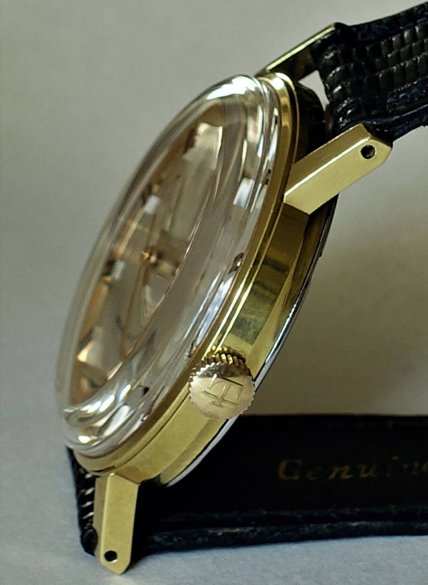 Goldfarbene Armbanduhr mit schwarzem Armband und transparenter Abdeckung.