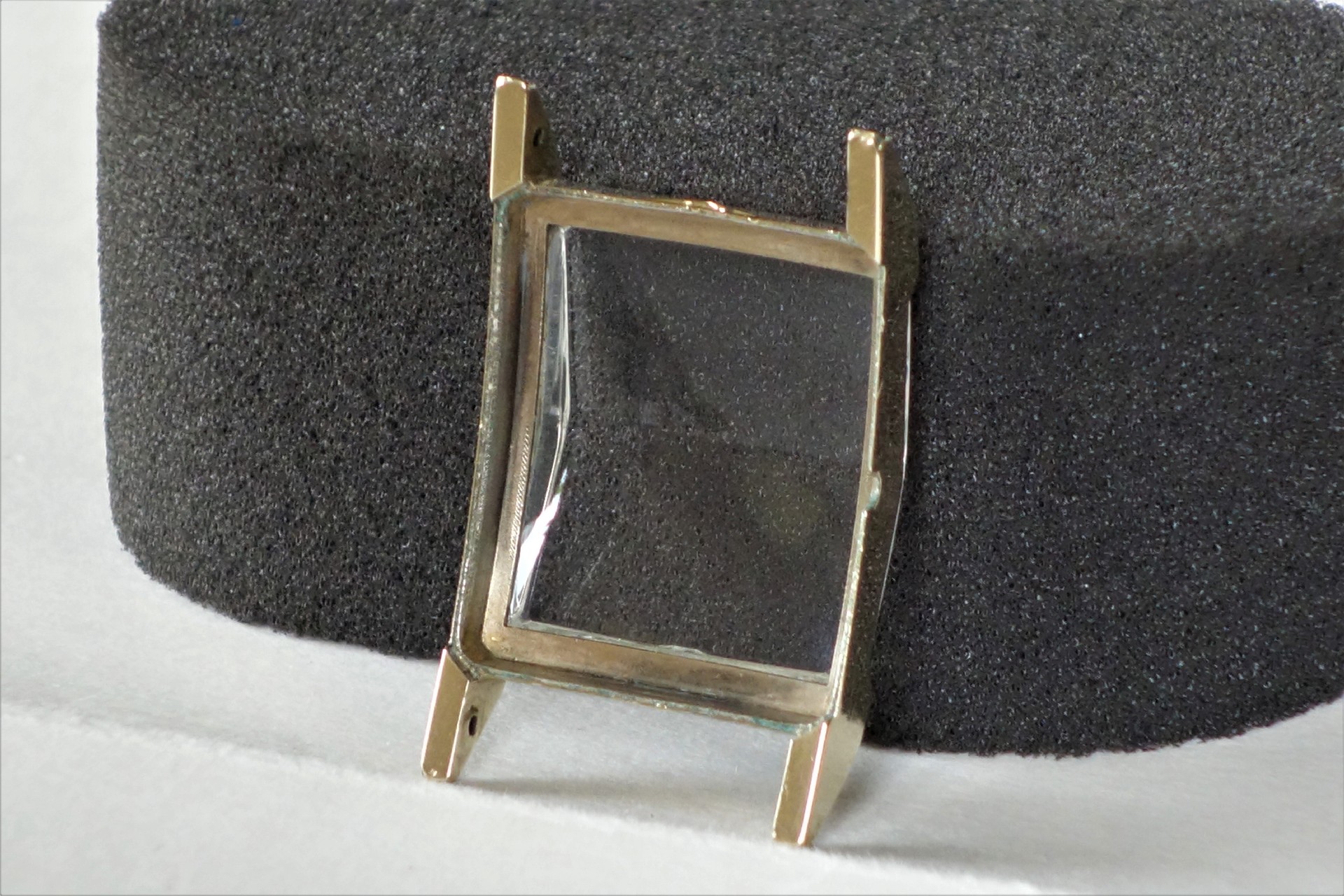 Eckiges, goldfarbenes Uhrengehäuse mit transparentem Glas.