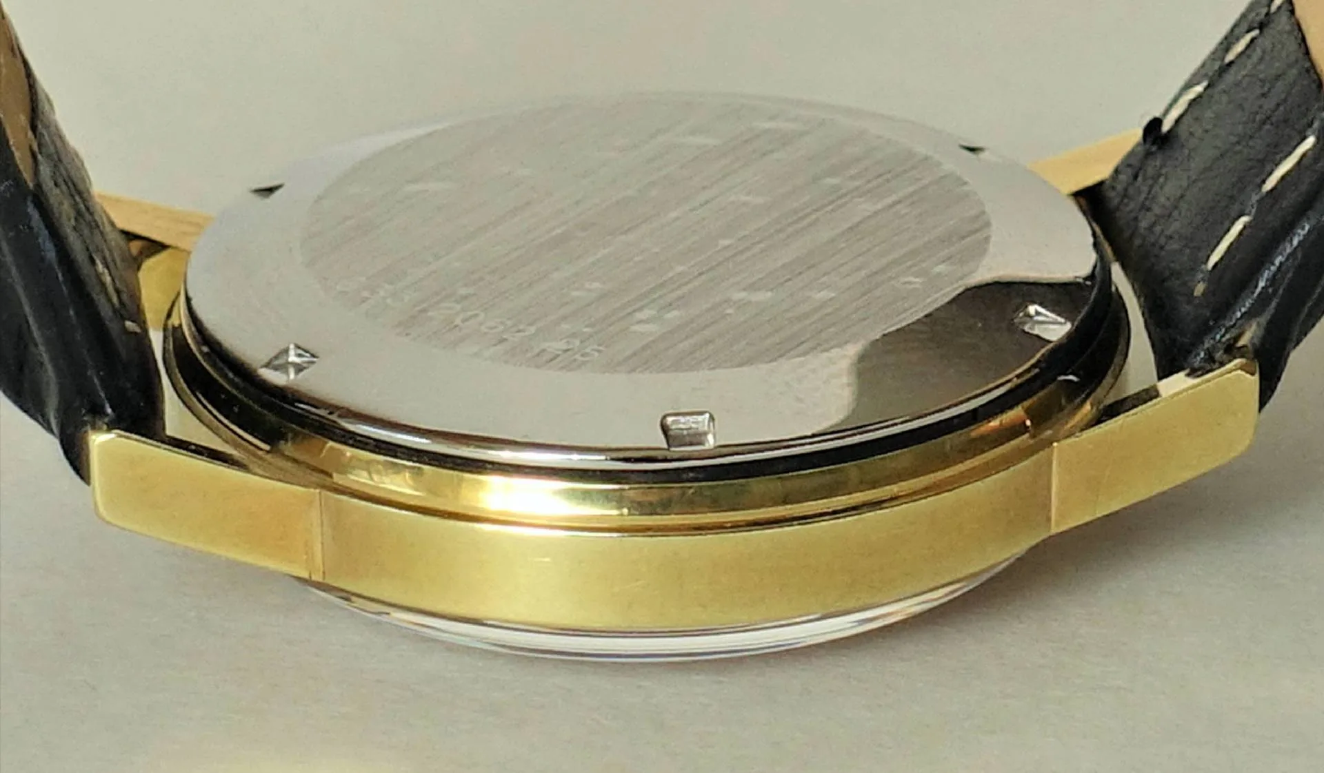 Silberfarbener Uhrenboden an einem Gehäuse mit goldfarbener Seite und schwarzem Armband.