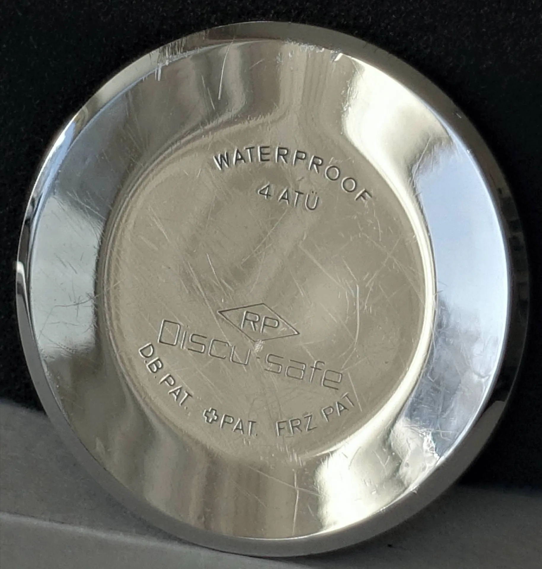 Uhrboden silberfarben Silberfarbener runder Uhrboden mit Gravur "Discus safe" und weiteren Angaben.