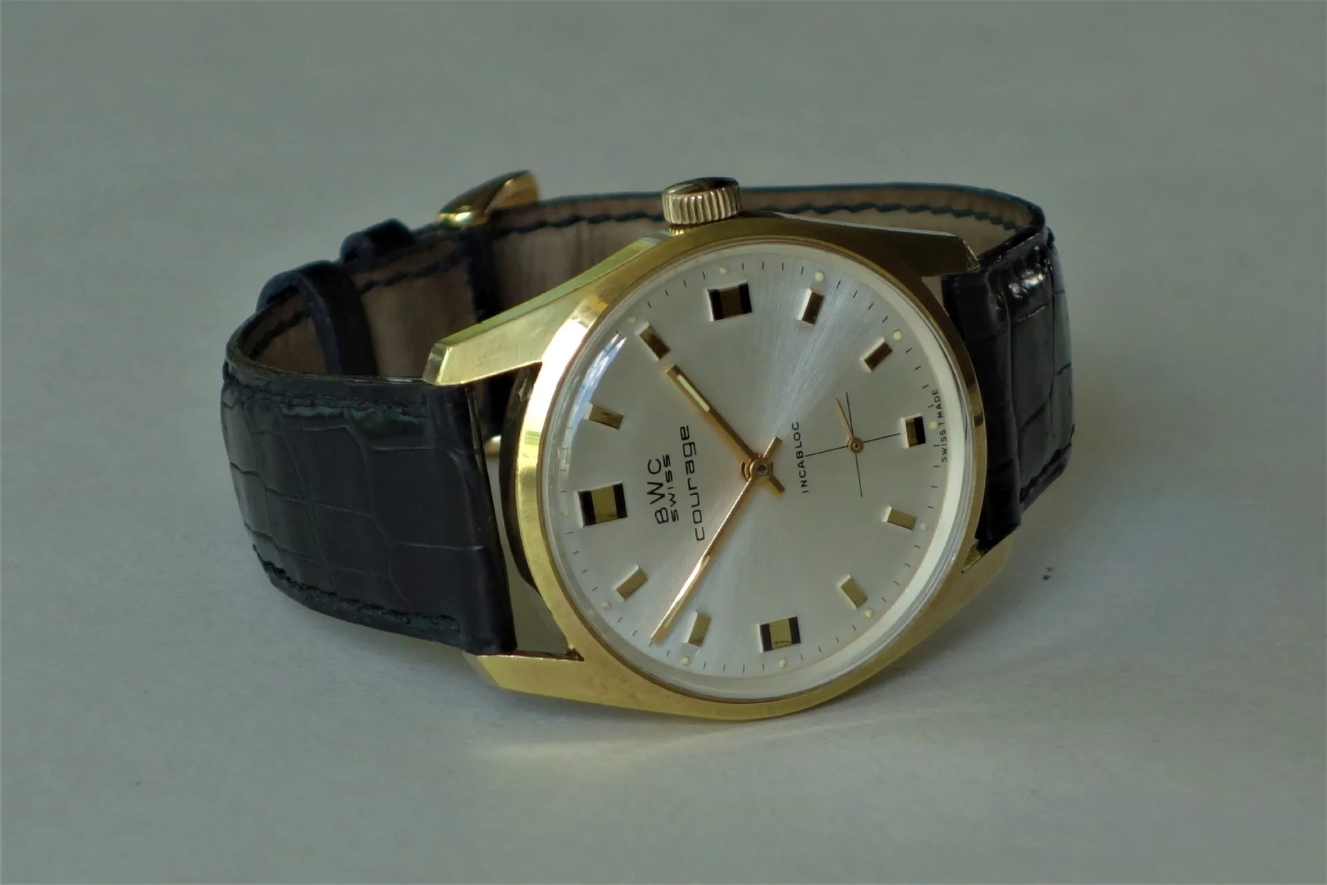 BWC Swiss Armbanduhr Analoge Armbanduhr mit goldfarbenem Gehäuse, silbernem Zifferblatt und schwarzem Lederarmband.