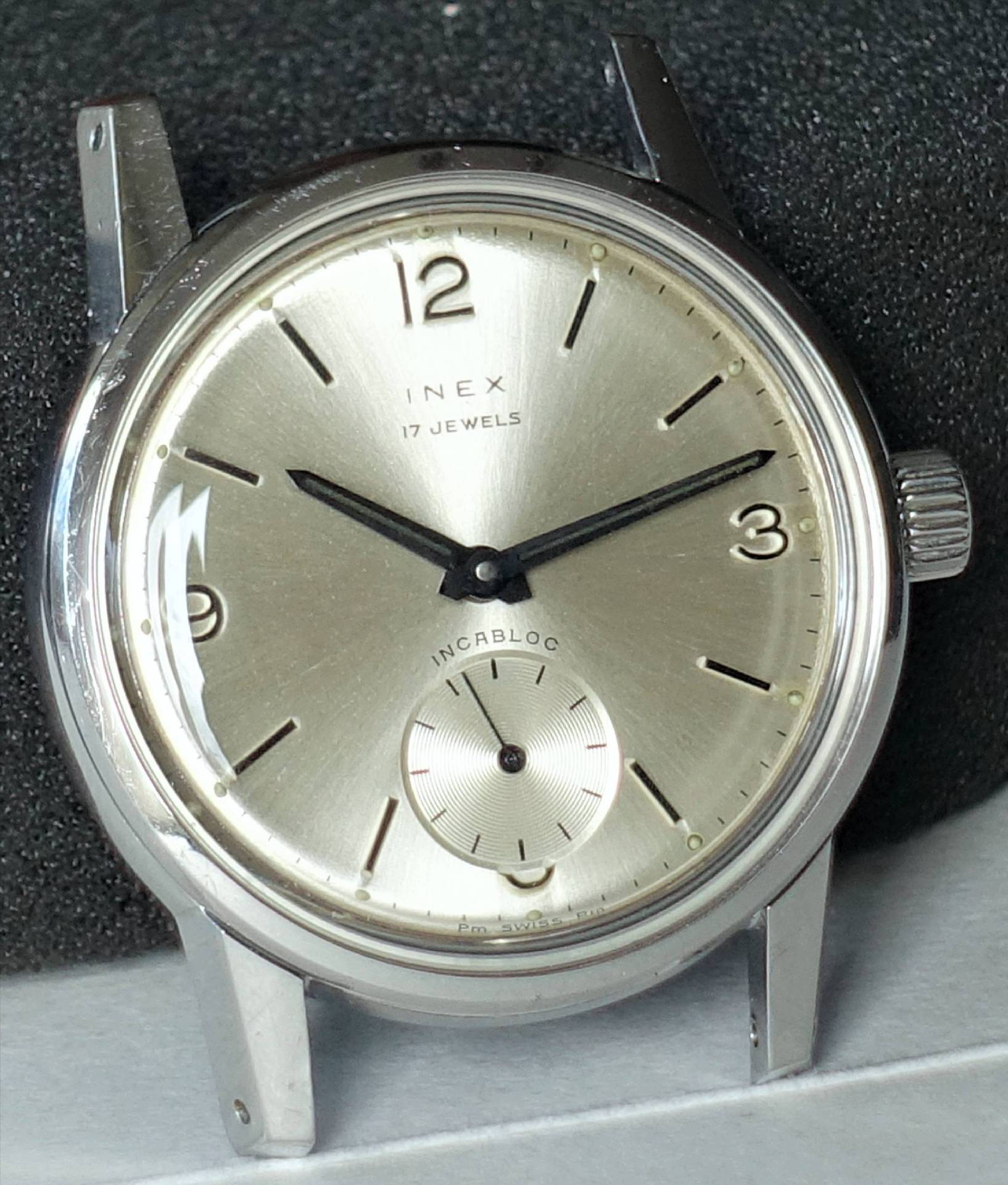 Nahaufnahme einer klassischen INEX Armbanduhr mit silbernem Zifferblatt und schwarzem Zeigerdesign.