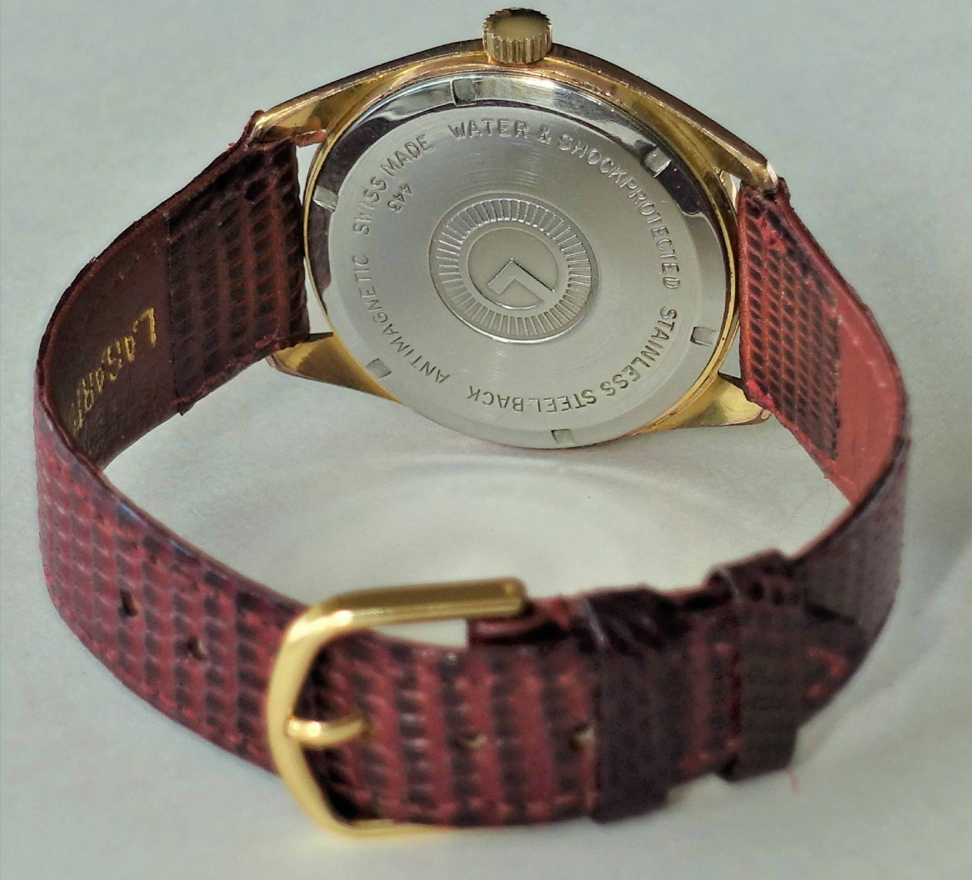 Rückseite einer Armbanduhr mit braunem Armband und goldfarbenem Gehäuse.