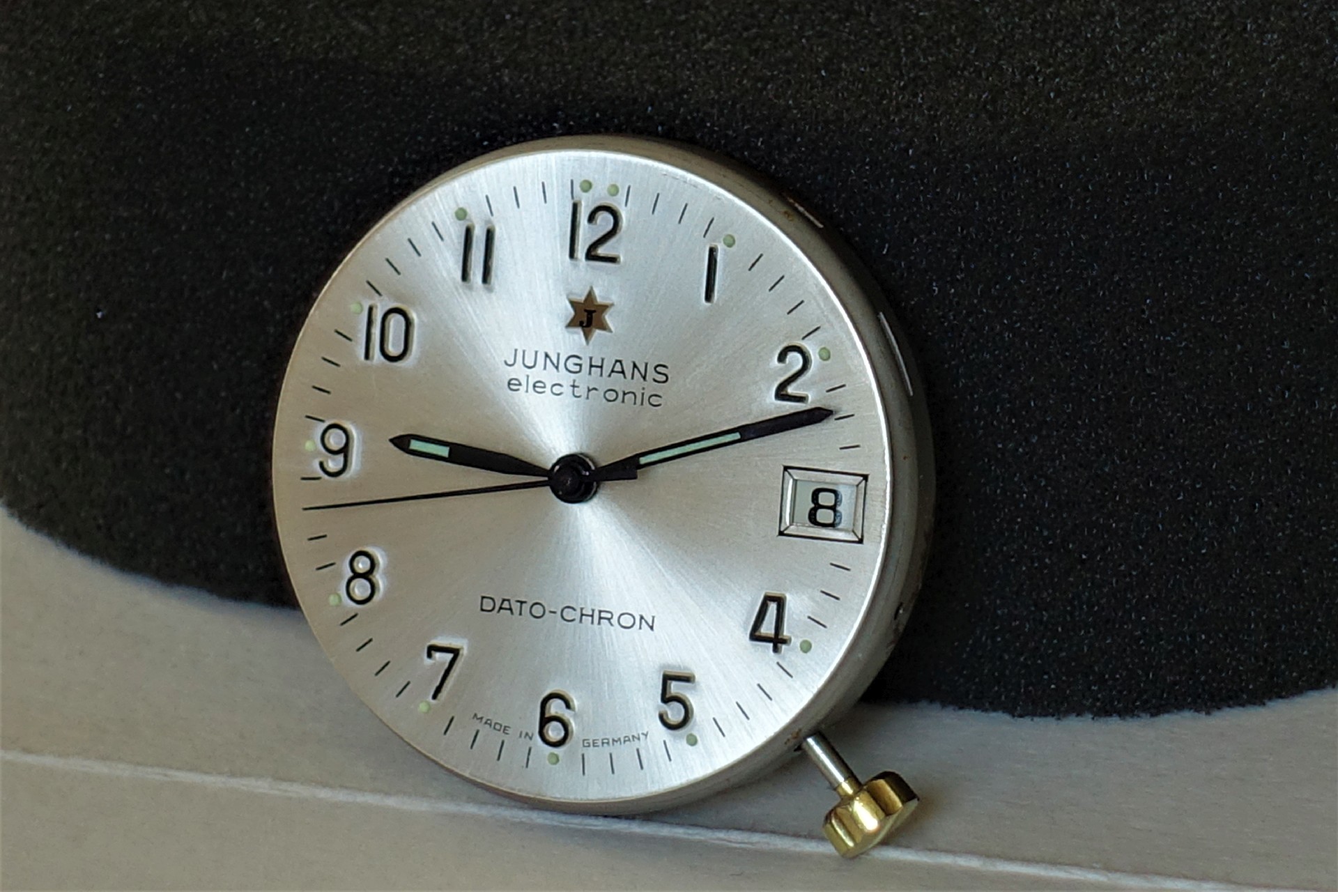 Silberfarbenes Junghans Uhrwerk mit Zifferblatt, Zeigern und Datumsanzeige.