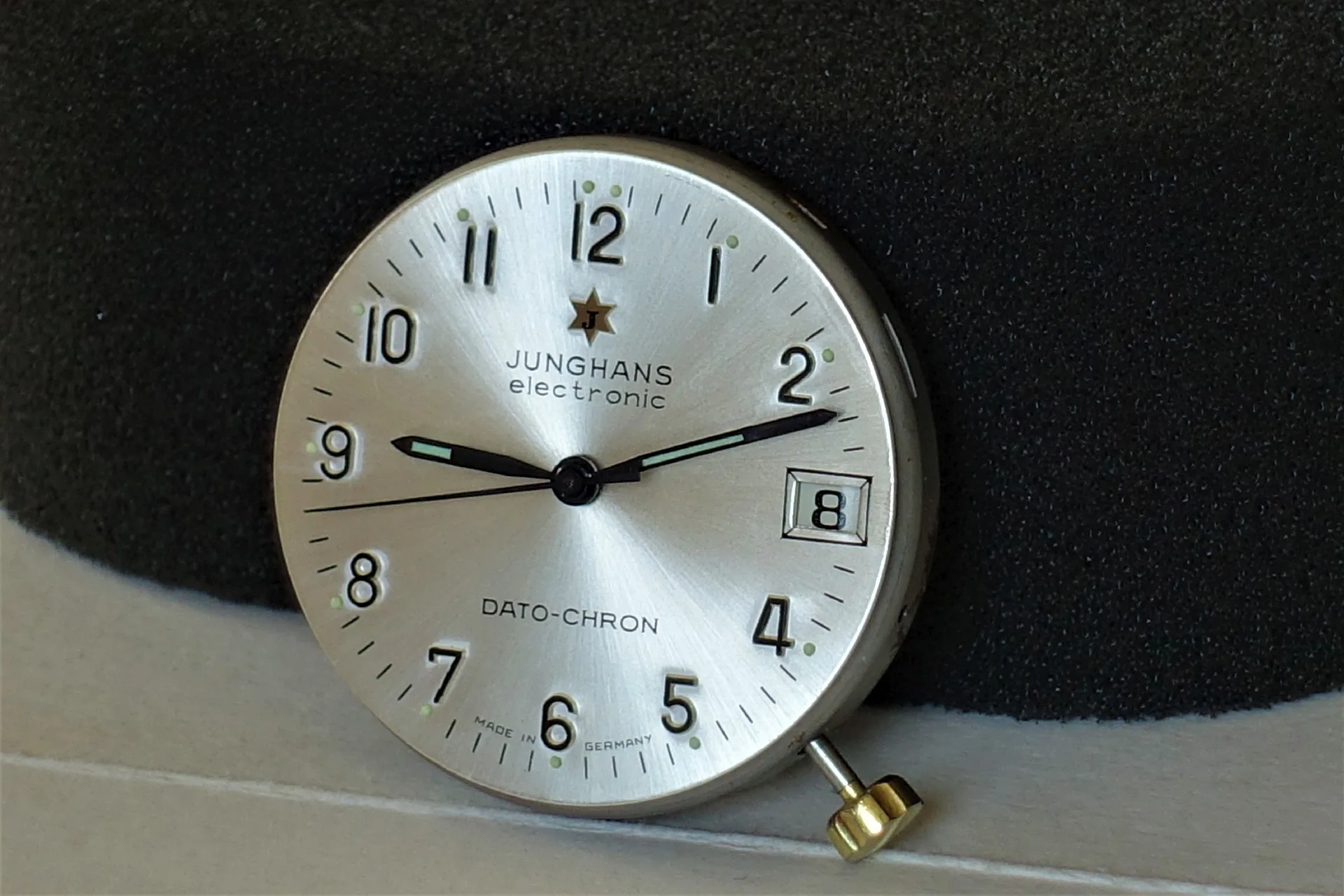 Silberfarbenes Junghans Uhrwerk mit Zifferblatt, Zeigern und Datumsanzeige.