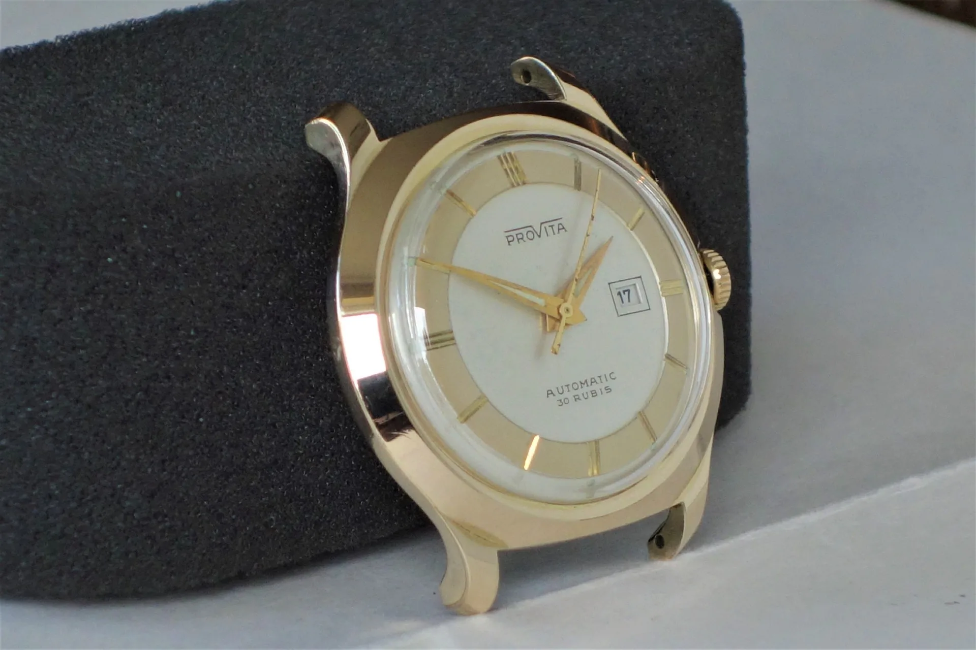 Runde Armbanduhr mit goldfarbenem Gehäuse und Zeigern, hellem Zifferblatt und Datumsanzeige.