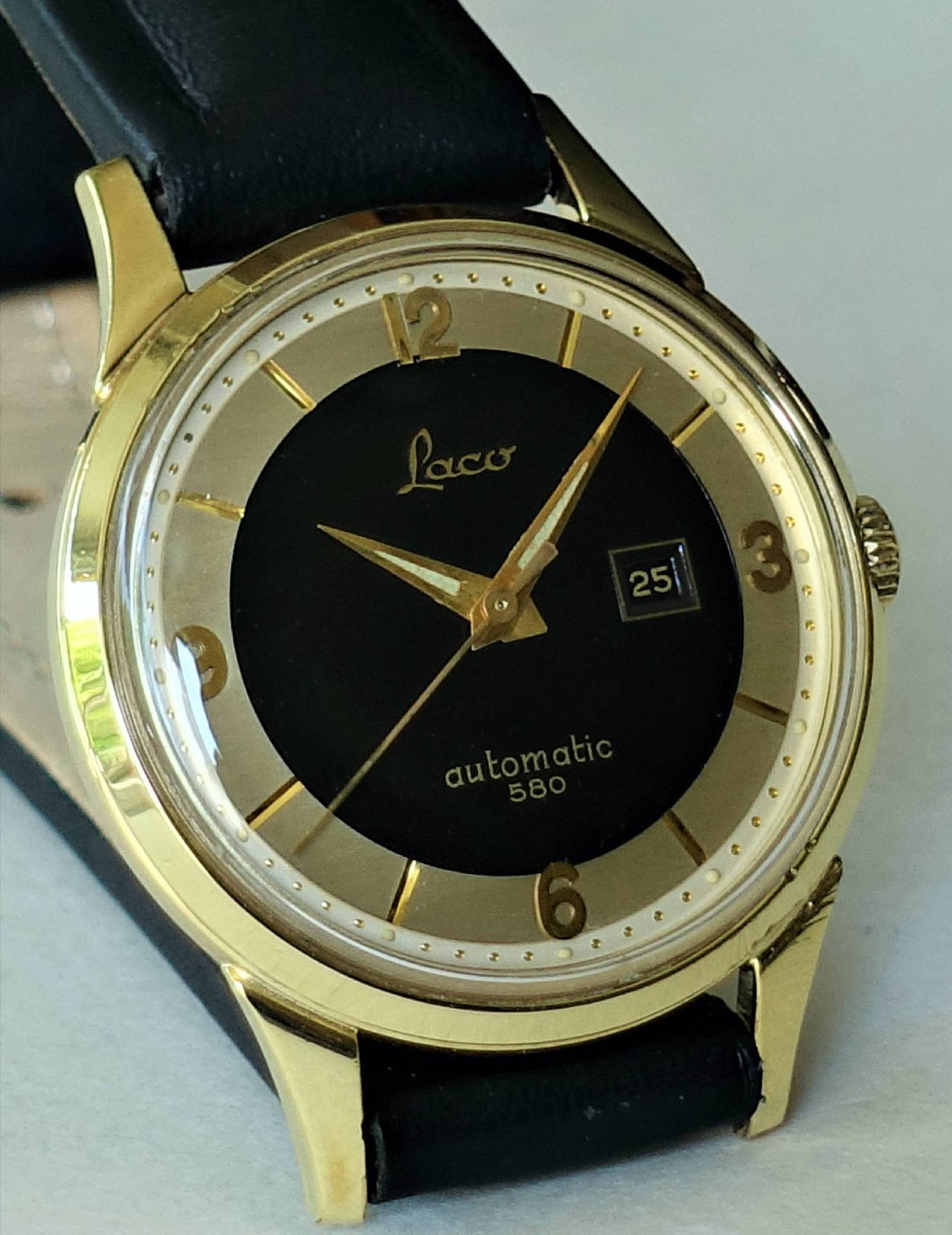 Goldfarbene Armbanduhr mit schwarzem Zifferblatt und schwarzem Armband.