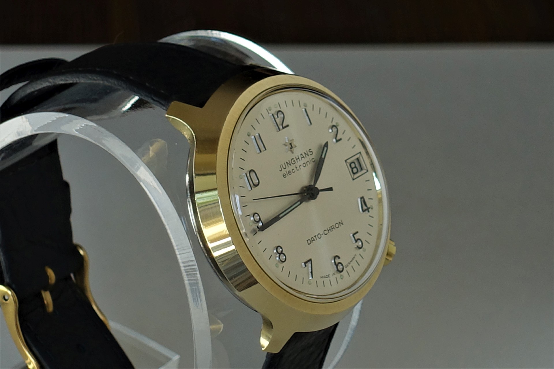 Helle Armbanduhr mit goldfarbenem Gehäuse, schwarzem Lederarmband und Datumsanzeige.