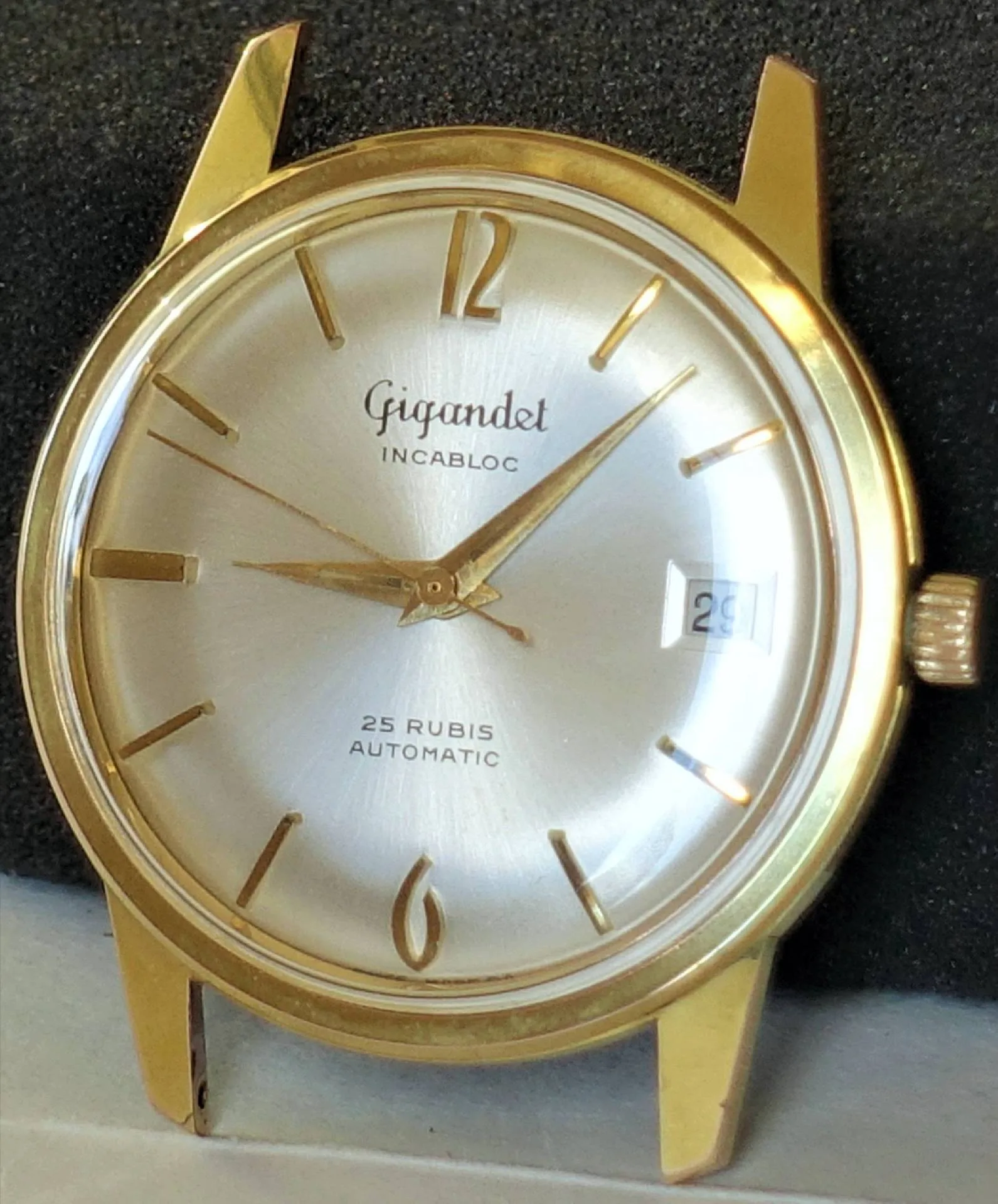Goldfarbene Vintage-Automatikuhr mit Datum Eine klassische Armbanduhr mit goldfarbenem Gehäuse, silberfarbenem Zifferblatt, goldfarbenen Zeigern und Indizes sowie Datumsanzeige bei drei Uhr.