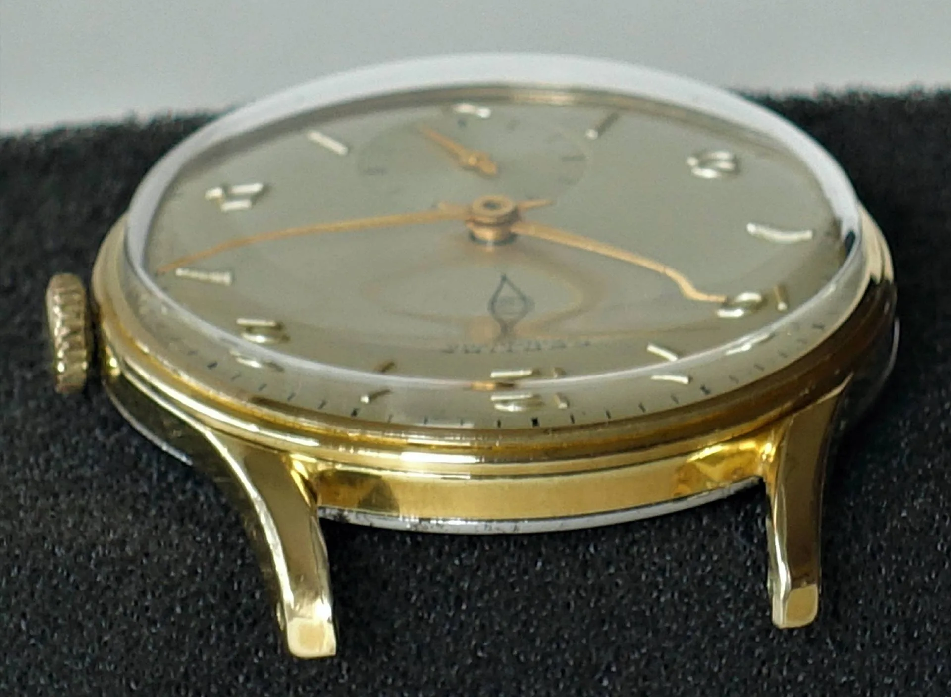 Flache Armbanduhr mit goldfarbenem Gehäuse und hellem Zifferblatt.