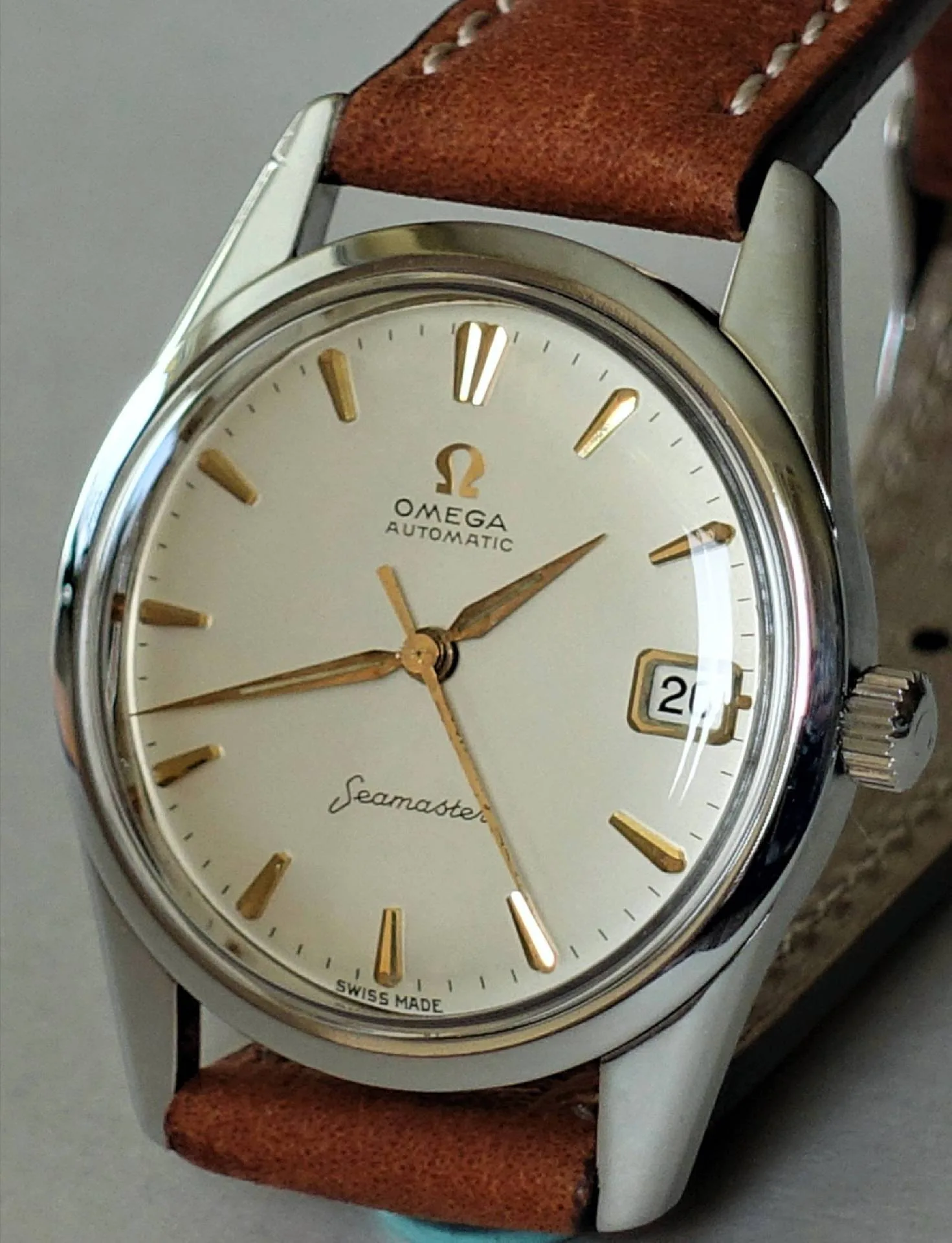 Omega Seamaster Armbanduhr Silberfarbene Armbanduhr mit beigem Zifferblatt, goldfarbenen Indizes und braunem Lederarmband.