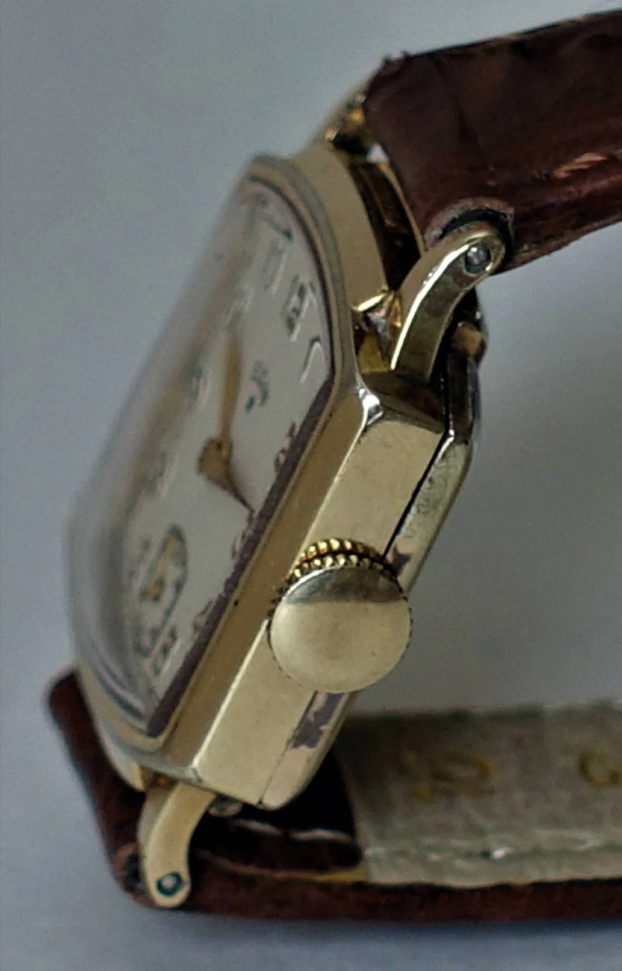 Rechteckige gelbgoldene Vintage-Uhr Seitliche Nahaufnahme einer rechteckigen Armbanduhr mit gelbgoldenem Gehäuse, cremefarbenem Zifferblatt und braunem Lederarmband.