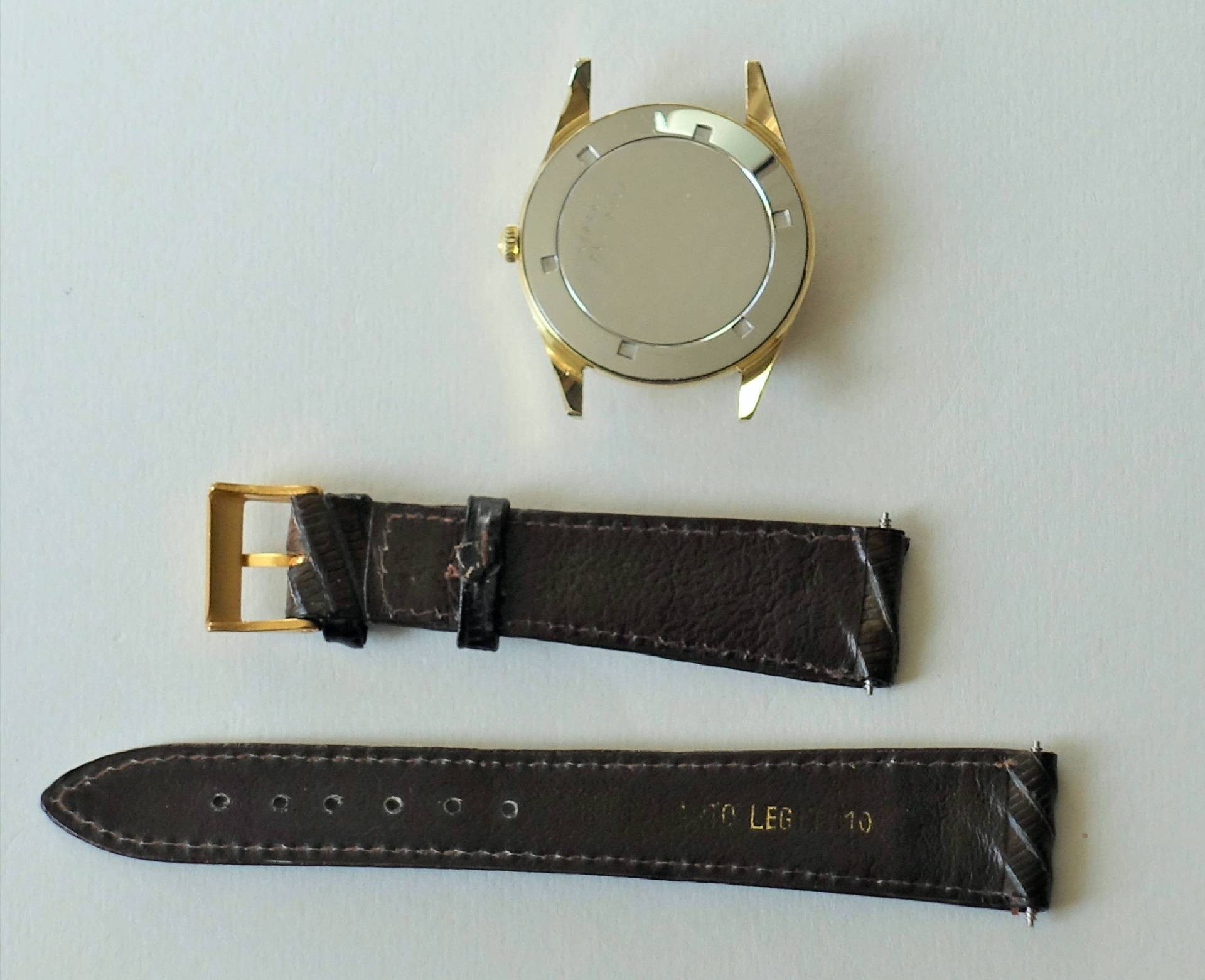 Zerlegtes goldfarbenes Uhrgehäuse mit braunem Lederarmband und goldfarbener Schließe.