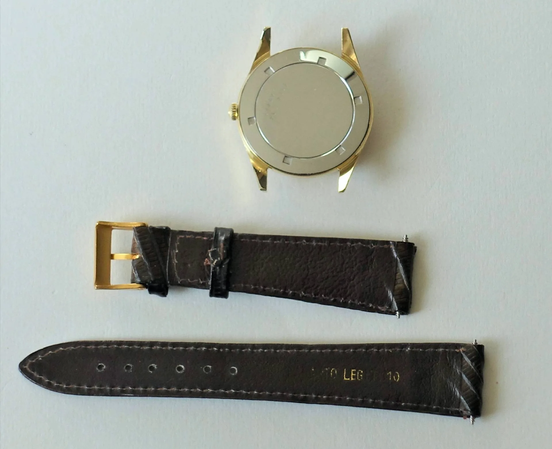 Uhrgehäuse goldfarben mit Lederarmband Zerlegtes goldfarbenes Uhrgehäuse mit braunem Lederarmband und goldfarbener Schließe.