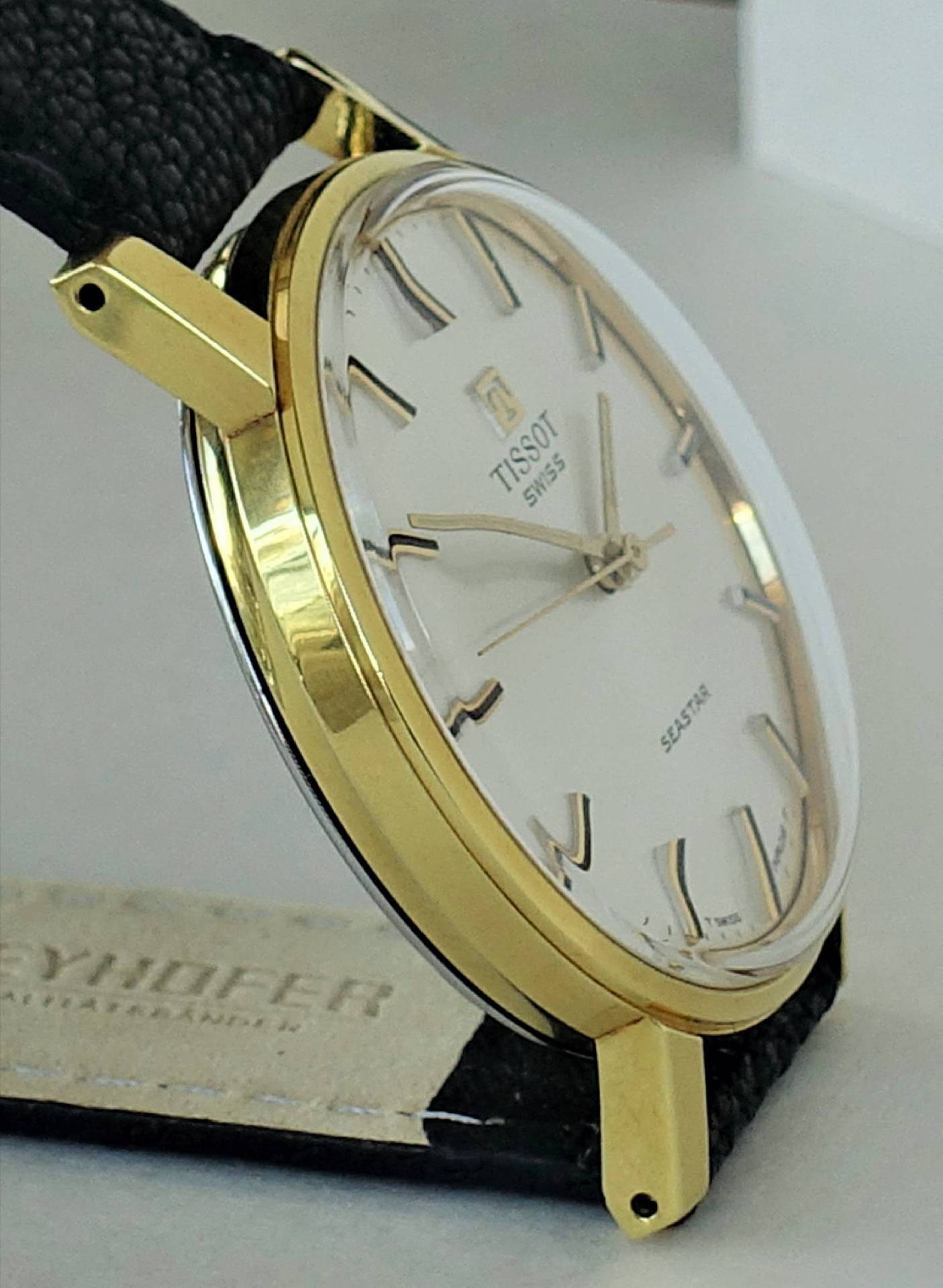 Goldfarbene Armbanduhr mit weißem Zifferblatt und schwarzem Armband.