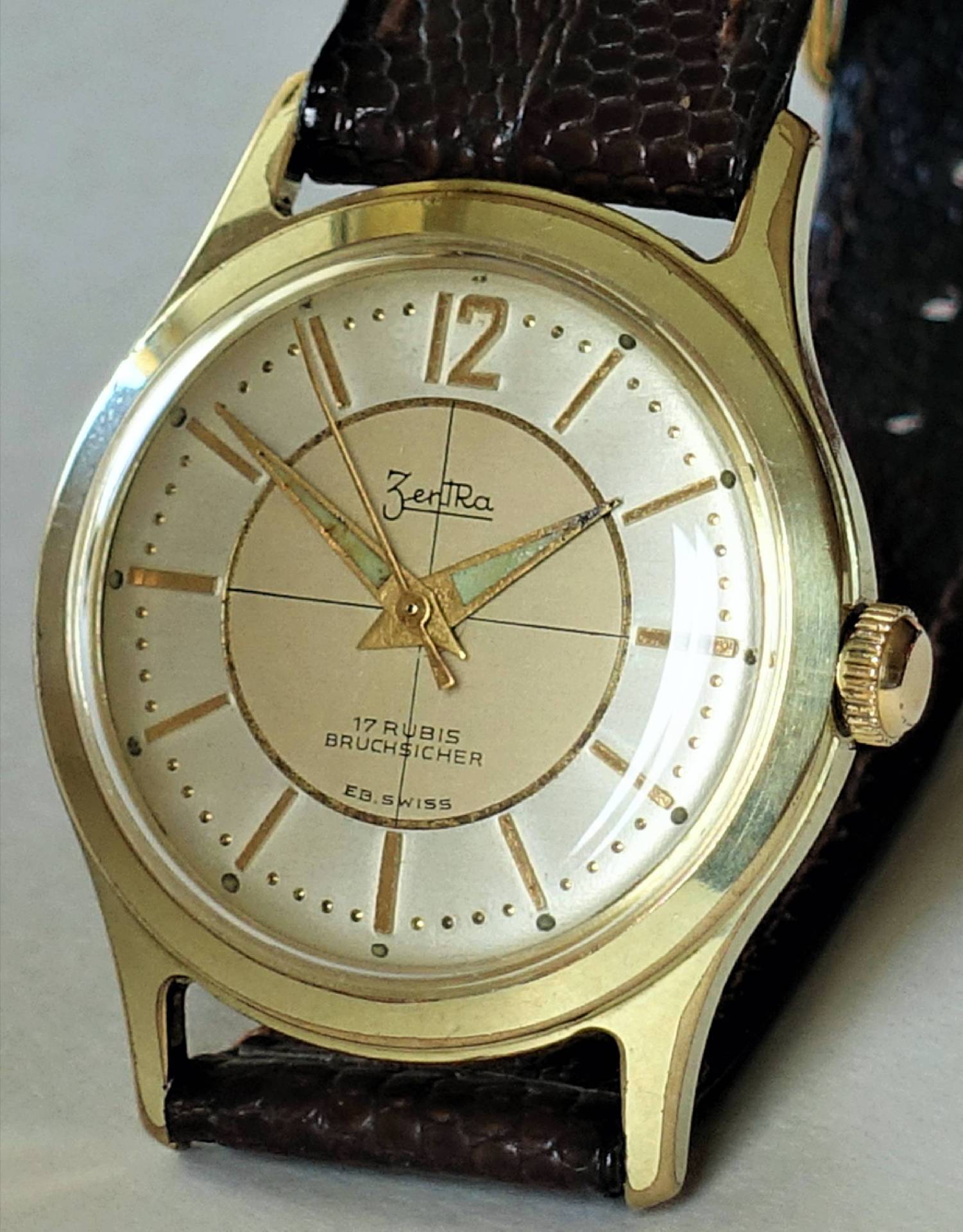 Goldfarbene Armbanduhr mit hellem Zifferblatt und braunem Armband.