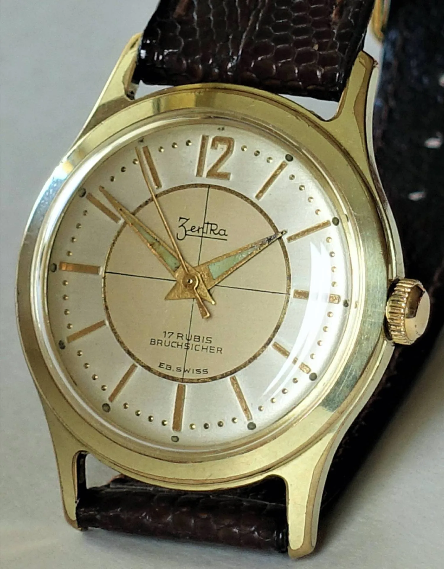 Goldfarbene Armbanduhr mit hellem Zifferblatt und braunem Armband.