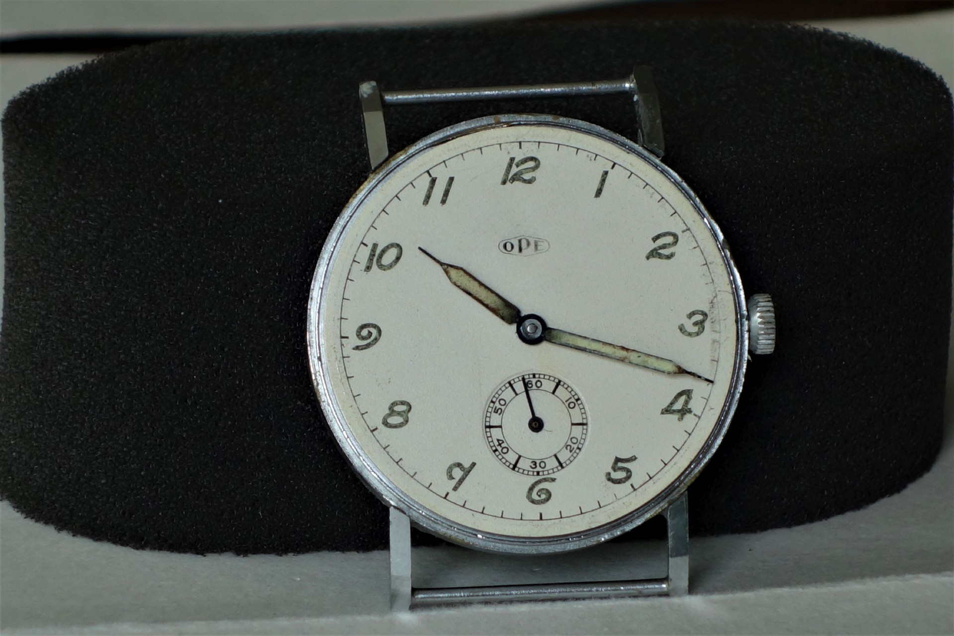 Runde mechanische Armbanduhr mit weißem Zifferblatt, schwarzen Ziffern und silberfarbenem Gehäuse.