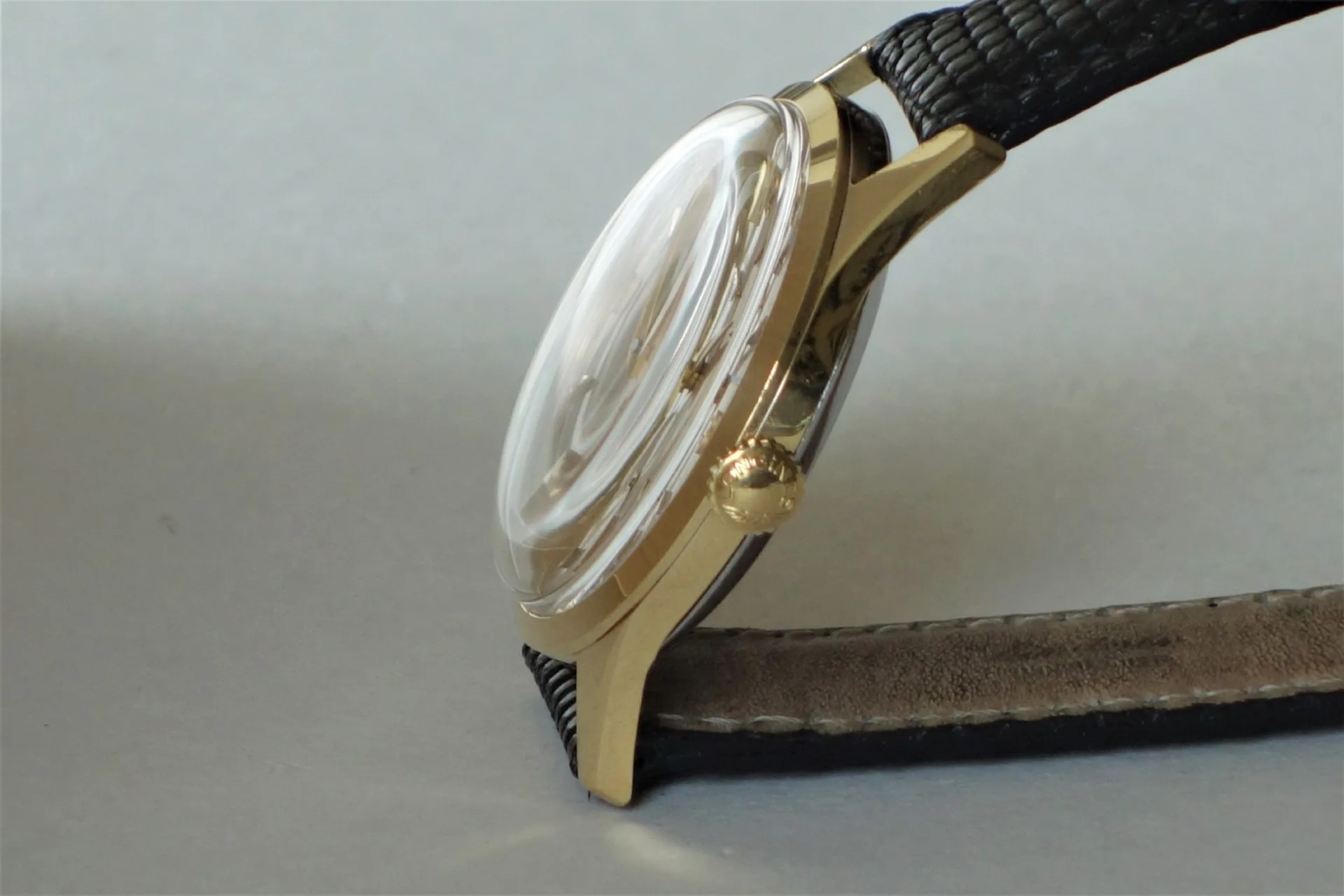 Goldfarbene Armbanduhr mit schwarzem Armband und gewölbtem Uhrglas.