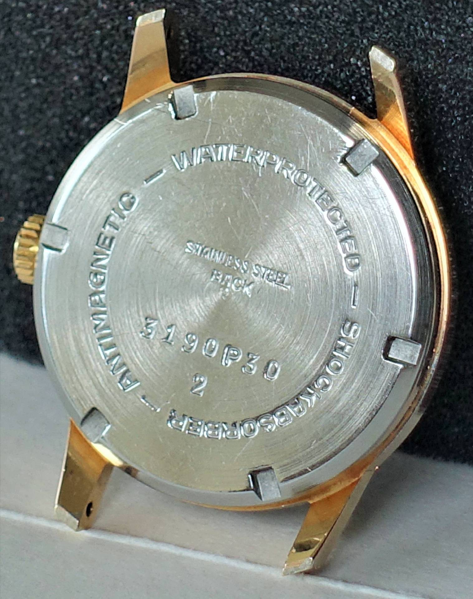 Rundes Uhrengehäuse mit silberfarbener Rückseite und goldfarbenen Hörnern.