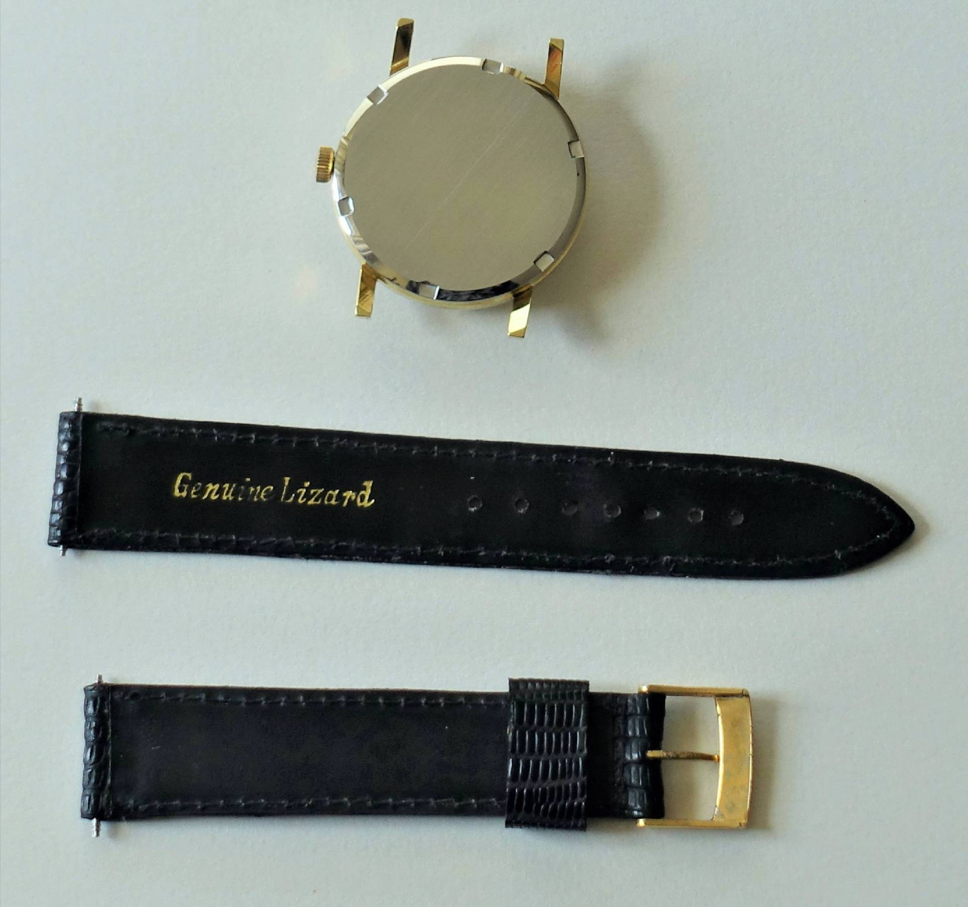 Rundes Uhrgehäuse in goldfarben mit schwarzem Lederarmband und goldfarbener Dornschließe.