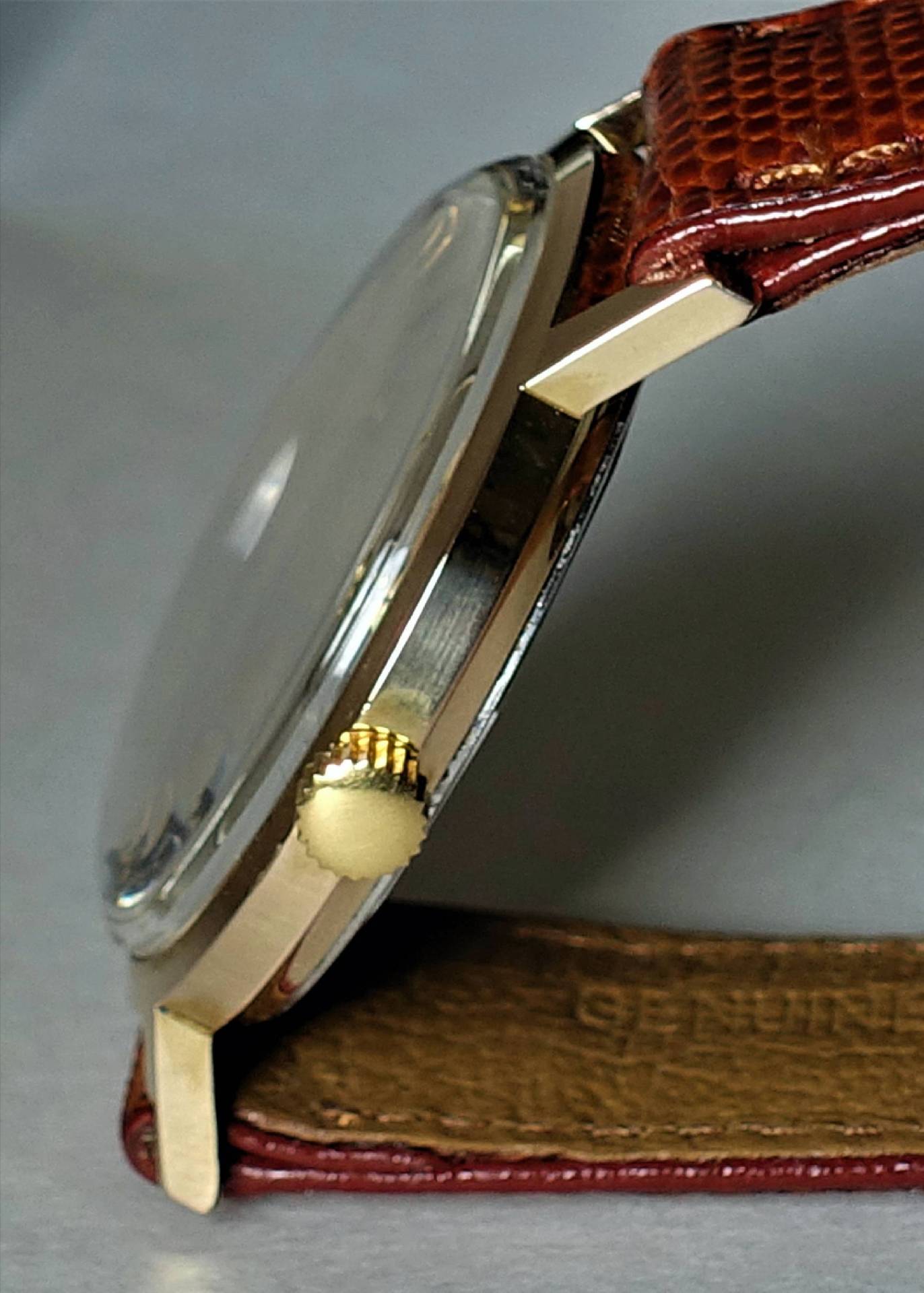 Flache Armbanduhr mit goldfarbenem Gehäuse, braunem Armband und goldfarbener Krone.