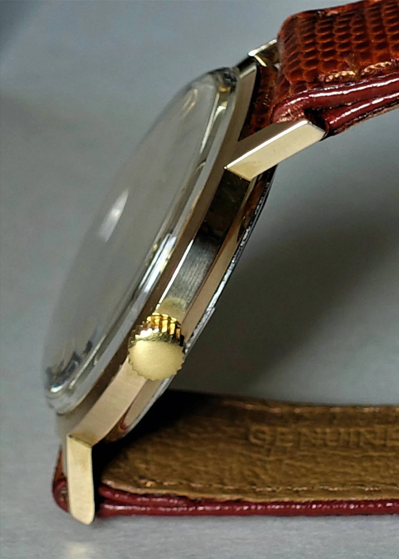 Flache Armbanduhr mit goldfarbenem Gehäuse, braunem Armband und goldfarbener Krone.