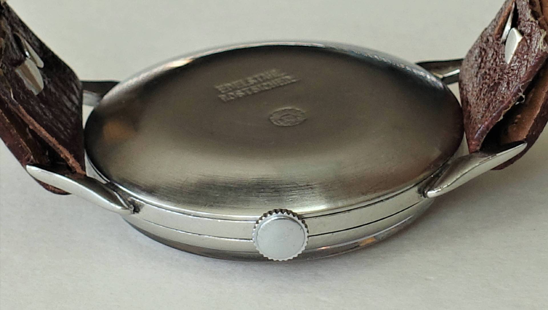 Rückseite einer silberfarbenen Armbanduhr mit braunem Lederarmband und seitlicher Krone.
