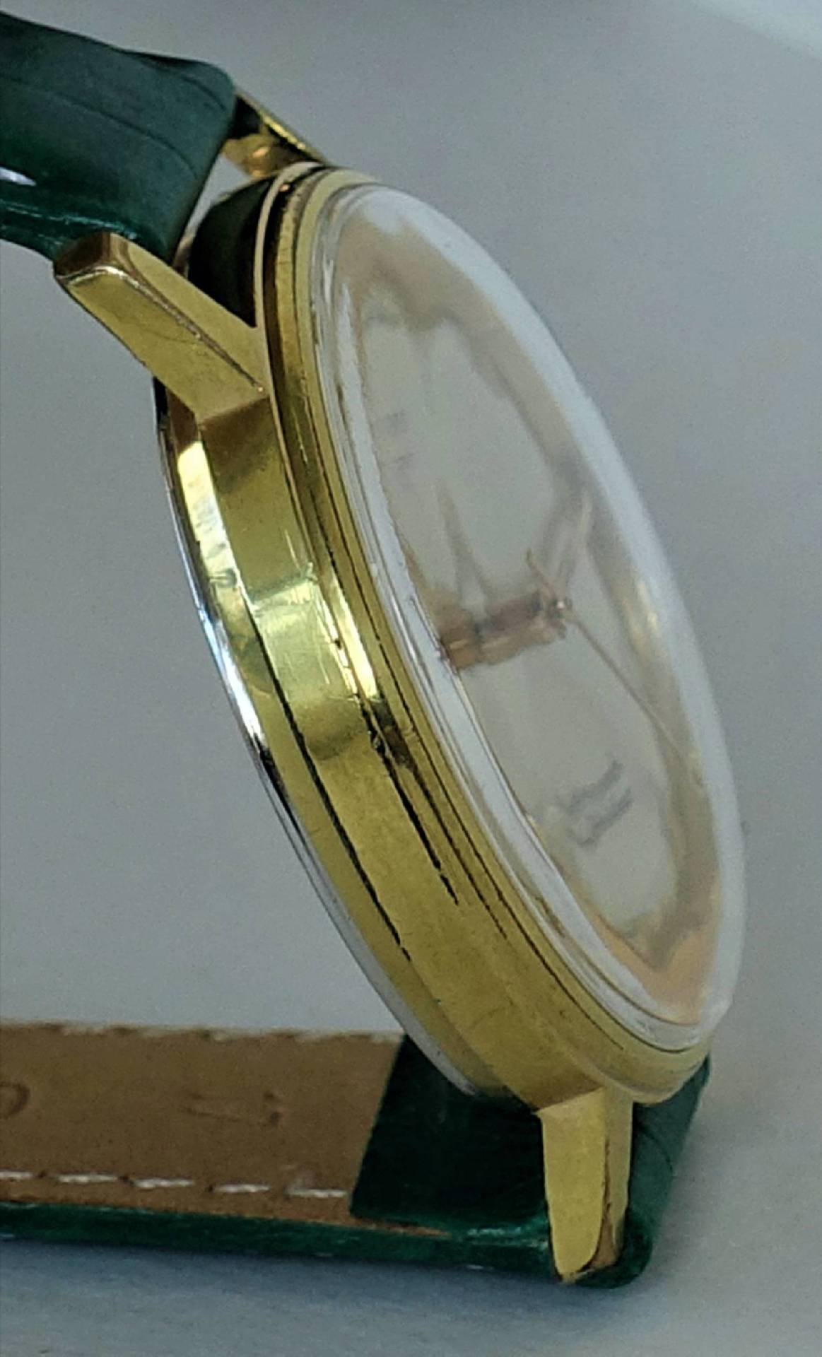 Goldfarbene Armbanduhr mit grünem Armband und hellem Zifferblatt.