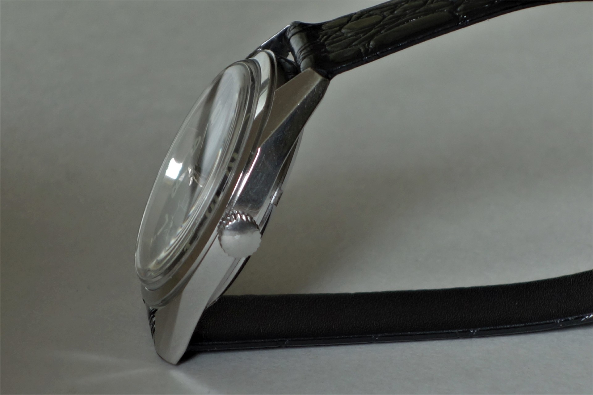 Seitliche Ansicht einer silberfarbenen Armbanduhr mit schwarzem Armband und transparenter Abdeckung.