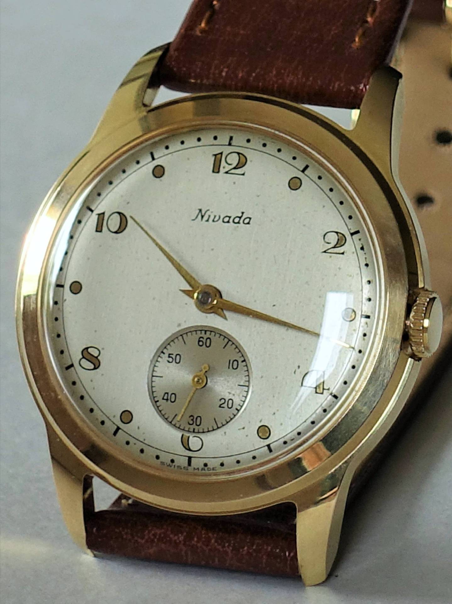 Goldfarbene Armbanduhr mit weißem Zifferblatt und braunem Armband.