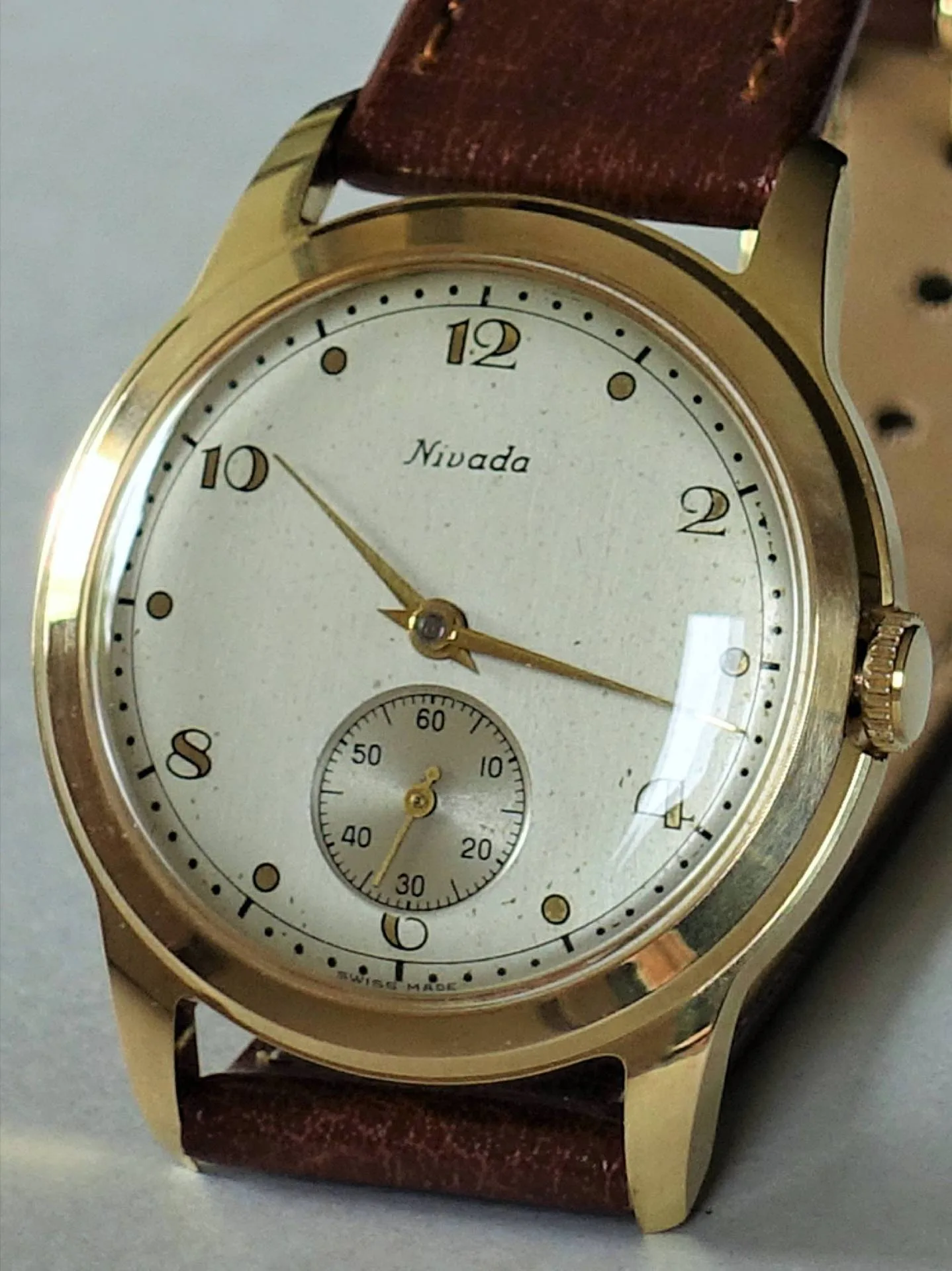 Goldfarbene Armbanduhr mit weißem Zifferblatt und braunem Armband.