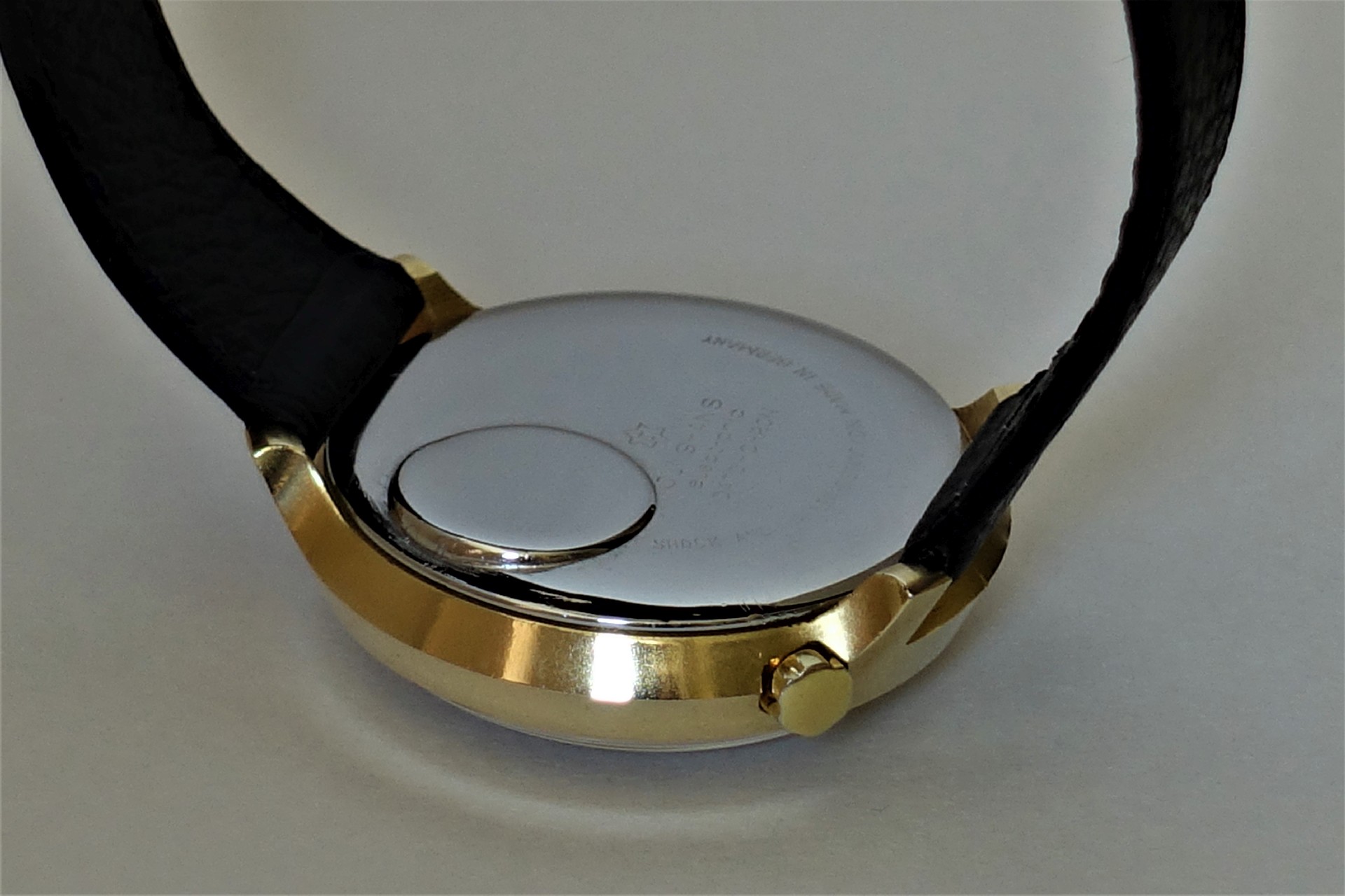 Silberfarbener Uhrenboden mit goldfarbener Gehäusekante und schwarzem Armband.