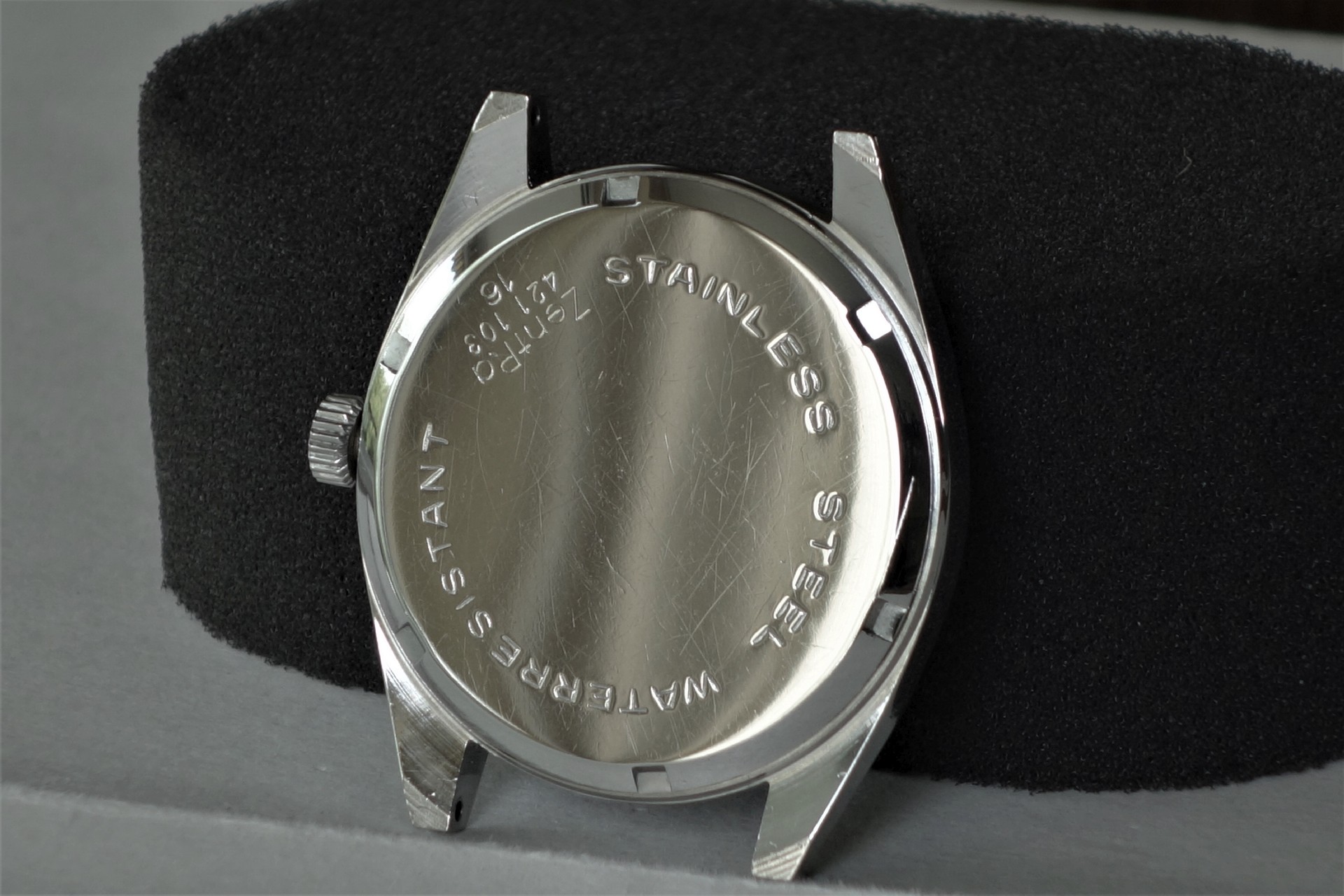 Silberfarbenes Uhrengehäuse mit verschraubtem Boden und seitlicher Krone.