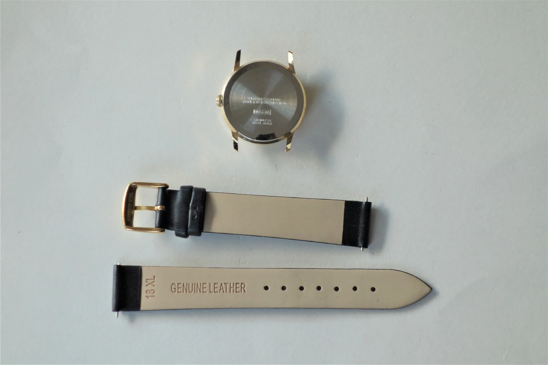 Goldfarbenes Uhrgehäuse mit schwarzem Lederarmband in zwei Teilen.