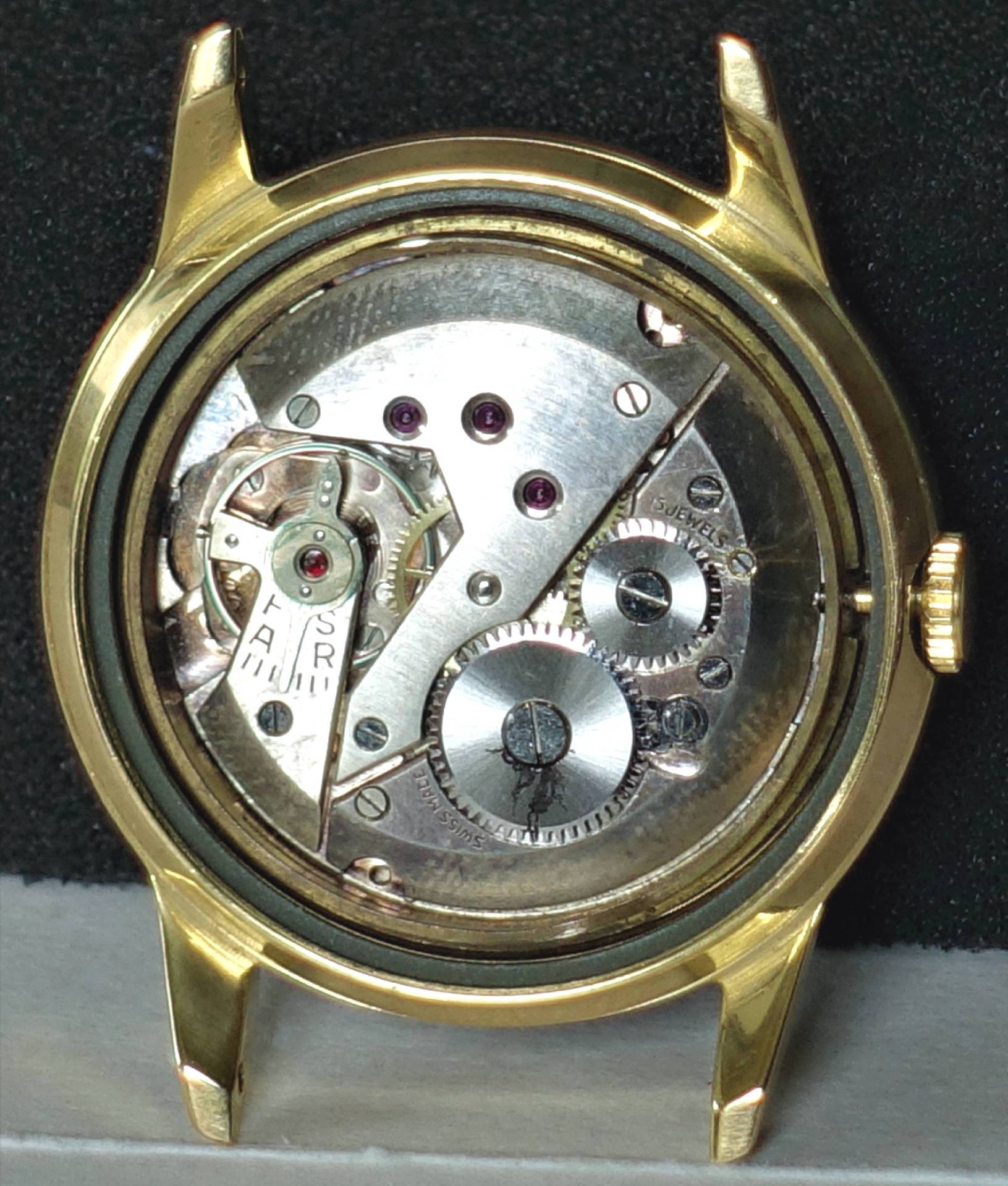 Offenes Uhrgehäuse in goldener Farbe mit sichtbarem mechanischem Uhrwerk.