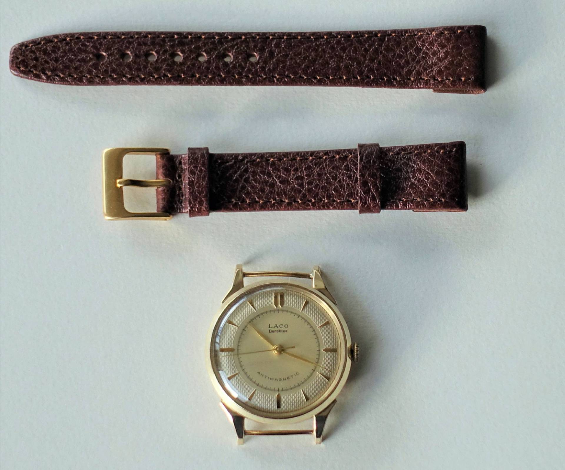Zerlegte Armbanduhr mit rundem, hellem Gehäuse und braunem Lederarmband.
