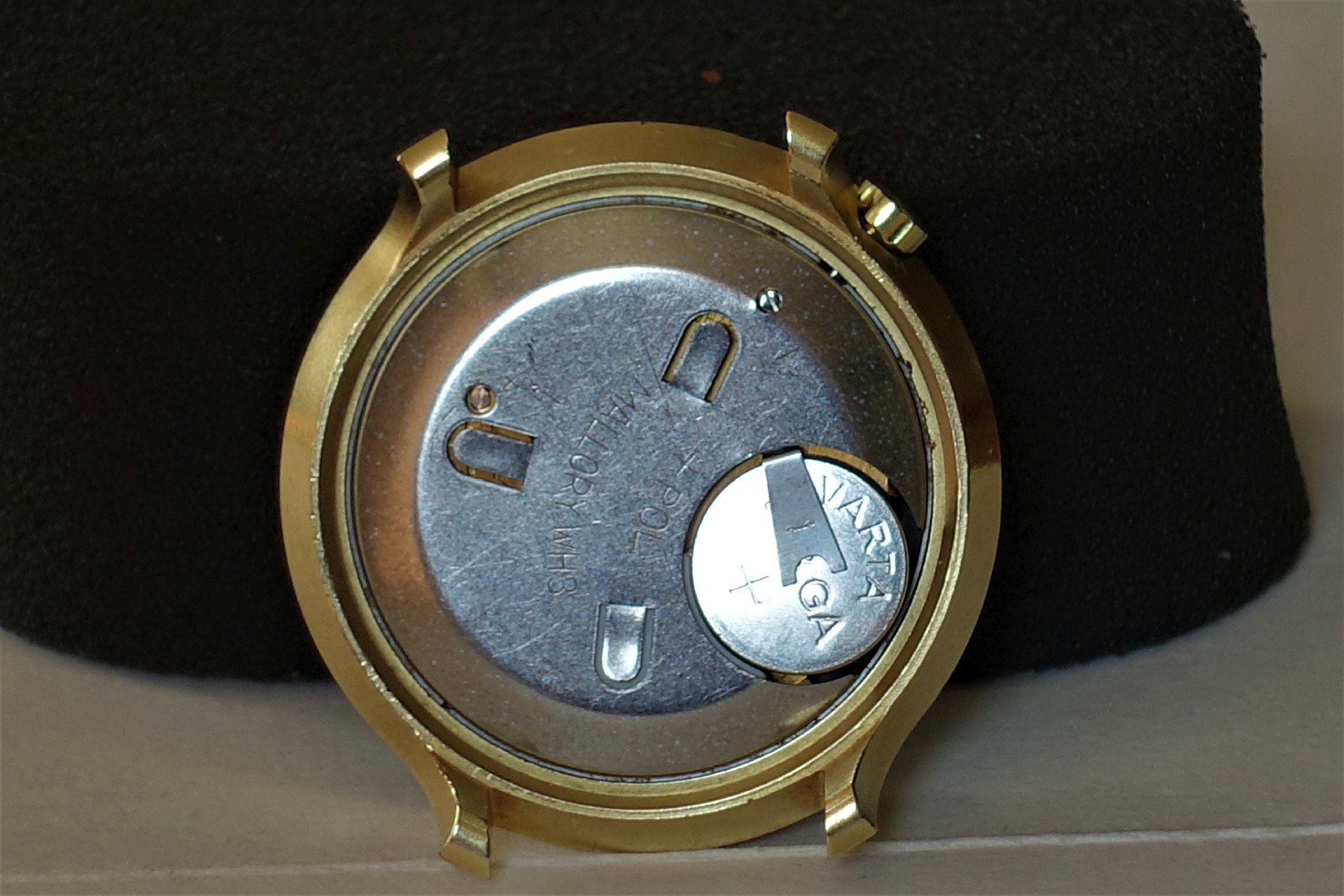 Silberfarbenes Quarzuhrwerk mit eingesetzter Knopfzelle in einem goldfarbenen Uhrengehäuse.