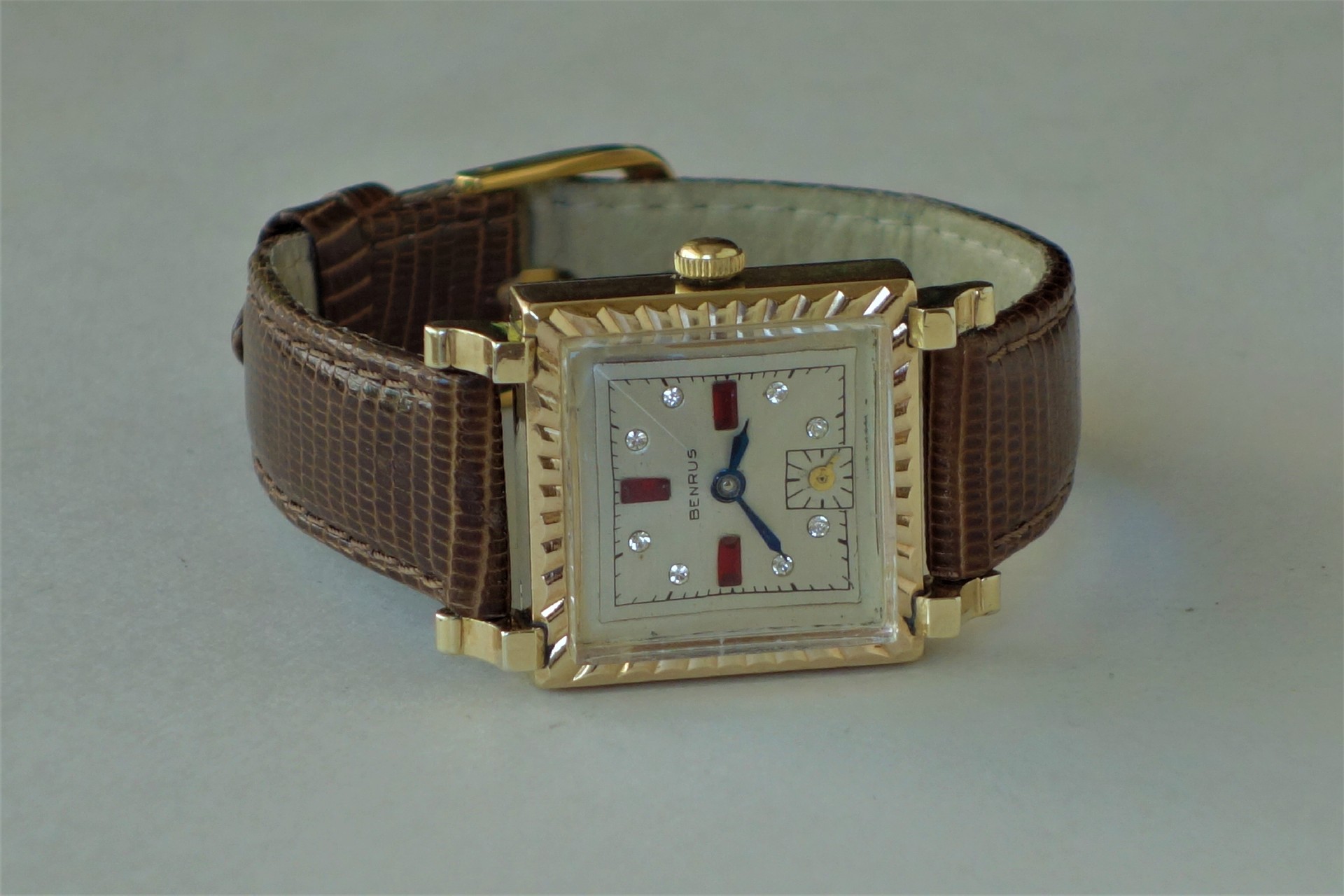 Rechteckige Armbanduhr mit goldfarbenem Gehäuse und braunem Lederarmband.