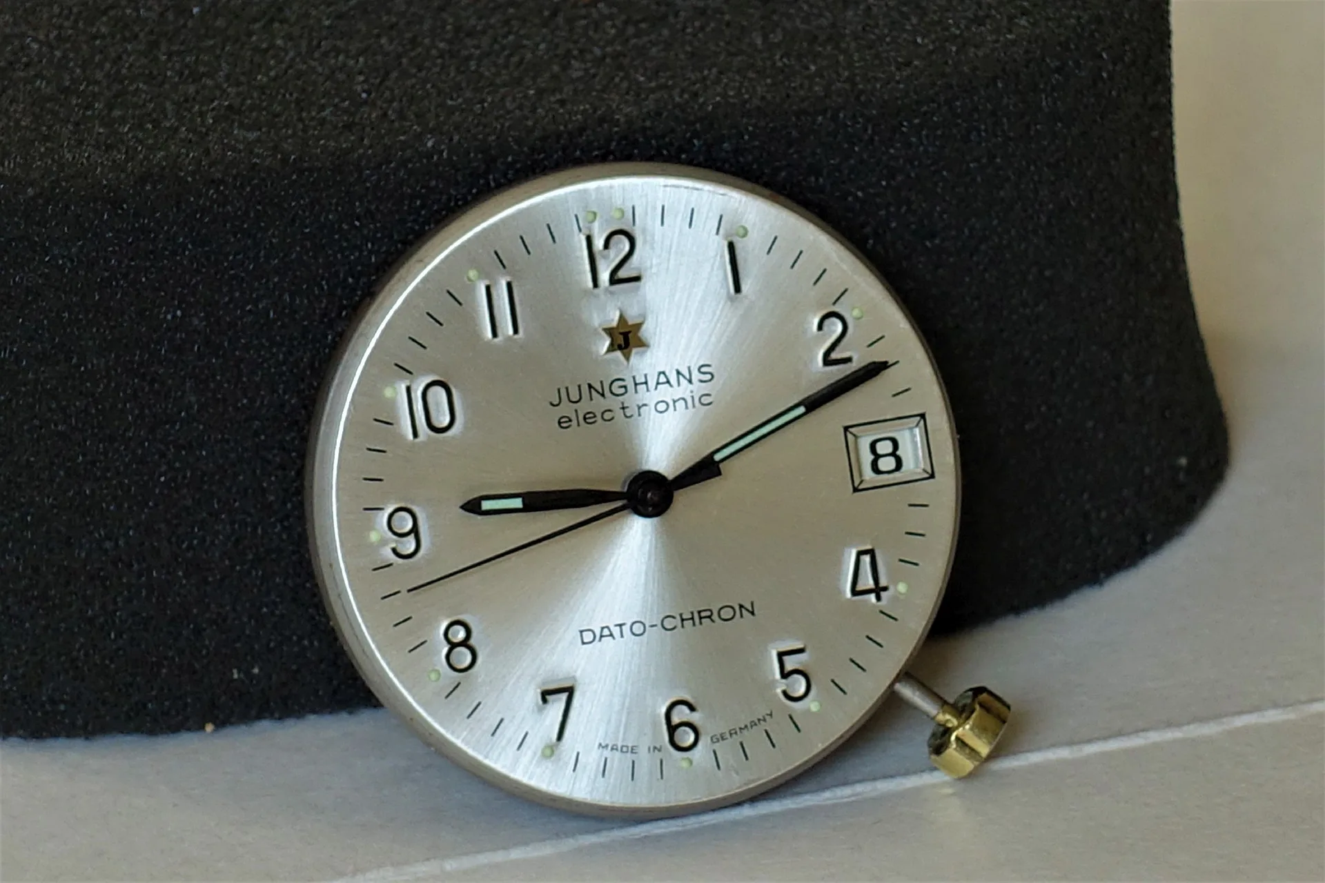 Junghans Dato-Chron Zifferblatt Silberfarbenes Zifferblatt einer Junghans Dato-Chron Uhr mit schwarzen Zeigern und Datumsanzeige.