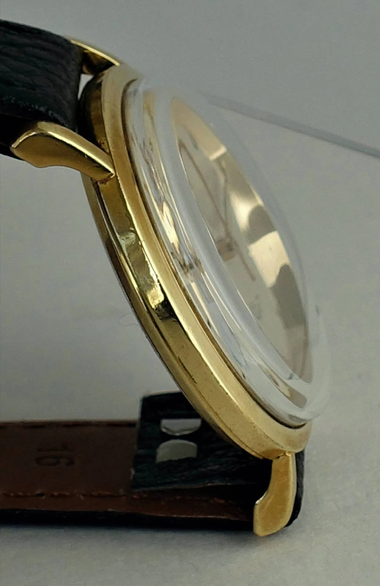 Uhrgehäuse goldfarben Seitliche Ansicht eines goldfarbenen Uhrgehäuses mit klarem Uhrglas und schwarzem Armband.