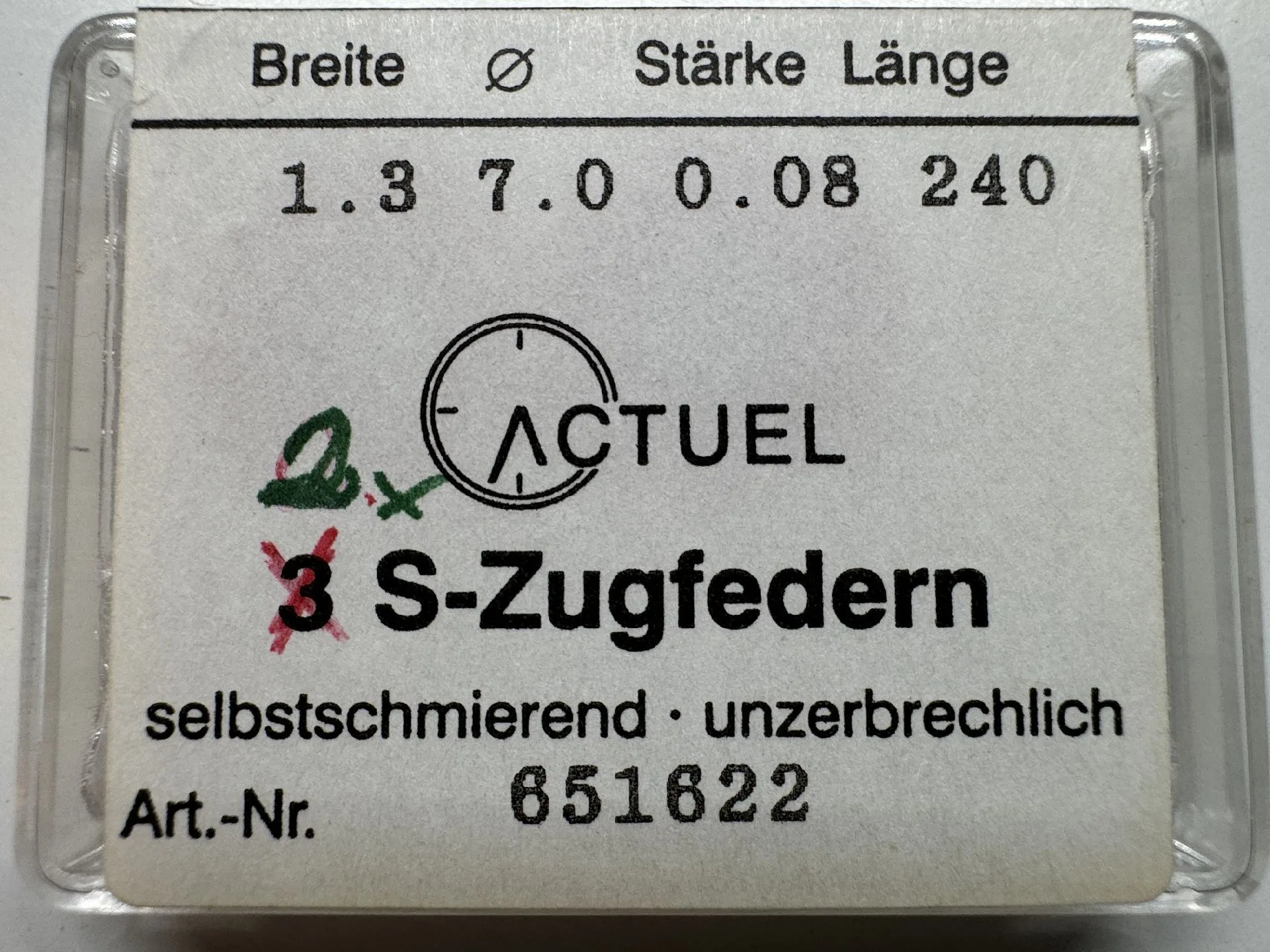 Verpackung mit einer Zugfeder für Uhrwerke, beschriftet mit technischen Angaben und Herstellername.