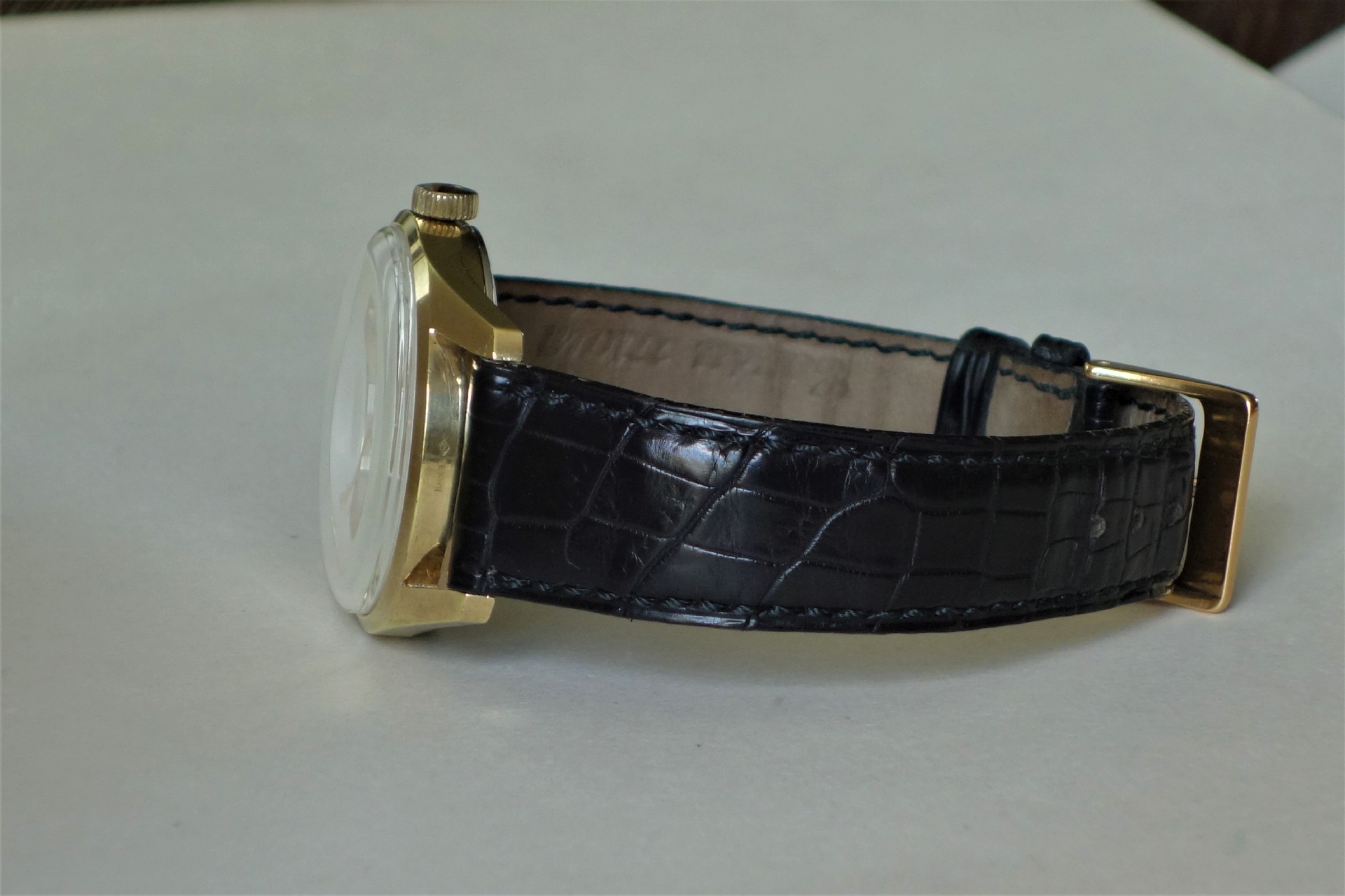Klassische Armbanduhr mit goldfarbenem Gehäuse und schwarzem Lederarmband mit Krokoprägung.
