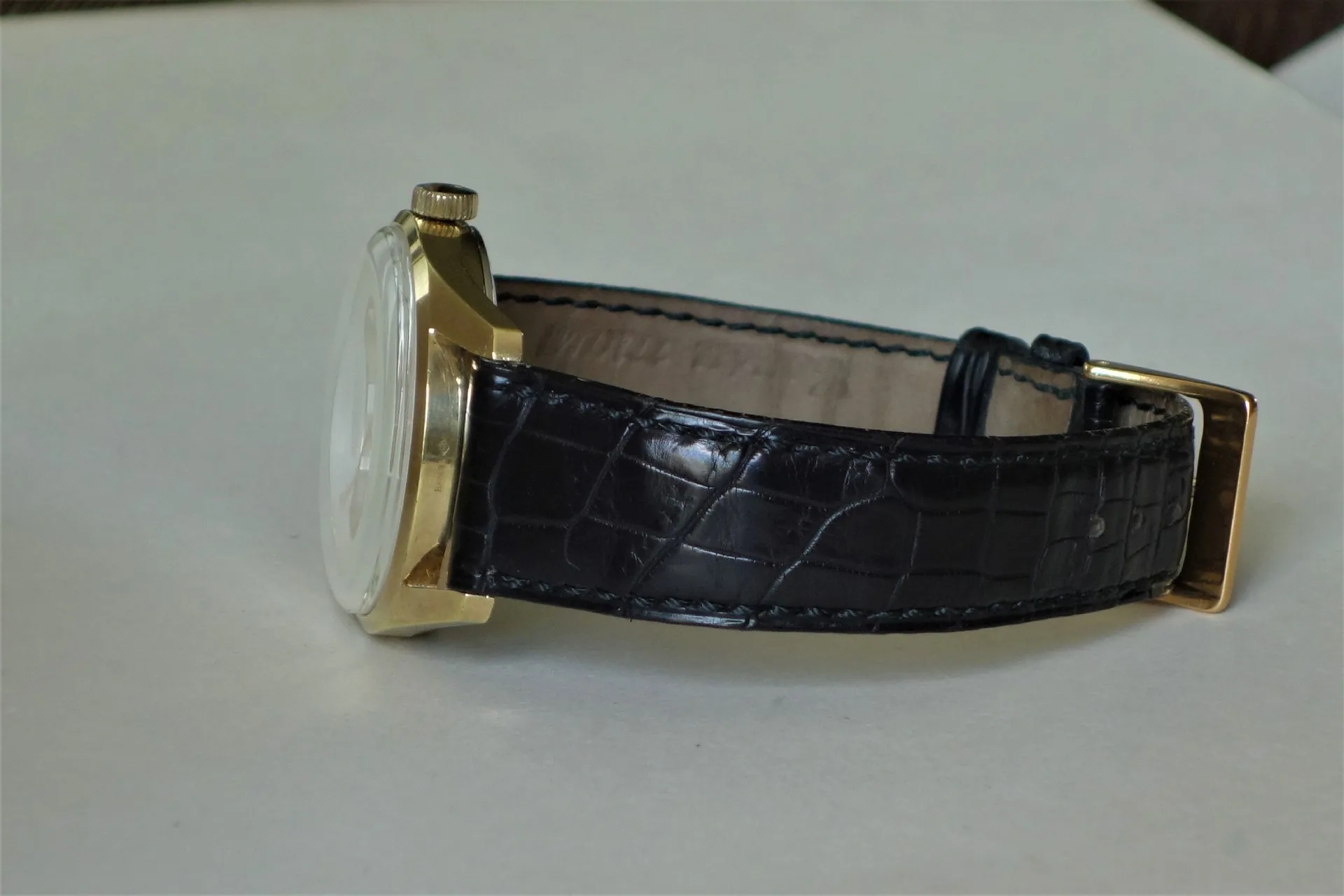 Klassische Armbanduhr mit goldfarbenem Gehäuse und schwarzem Lederarmband mit Krokoprägung.
