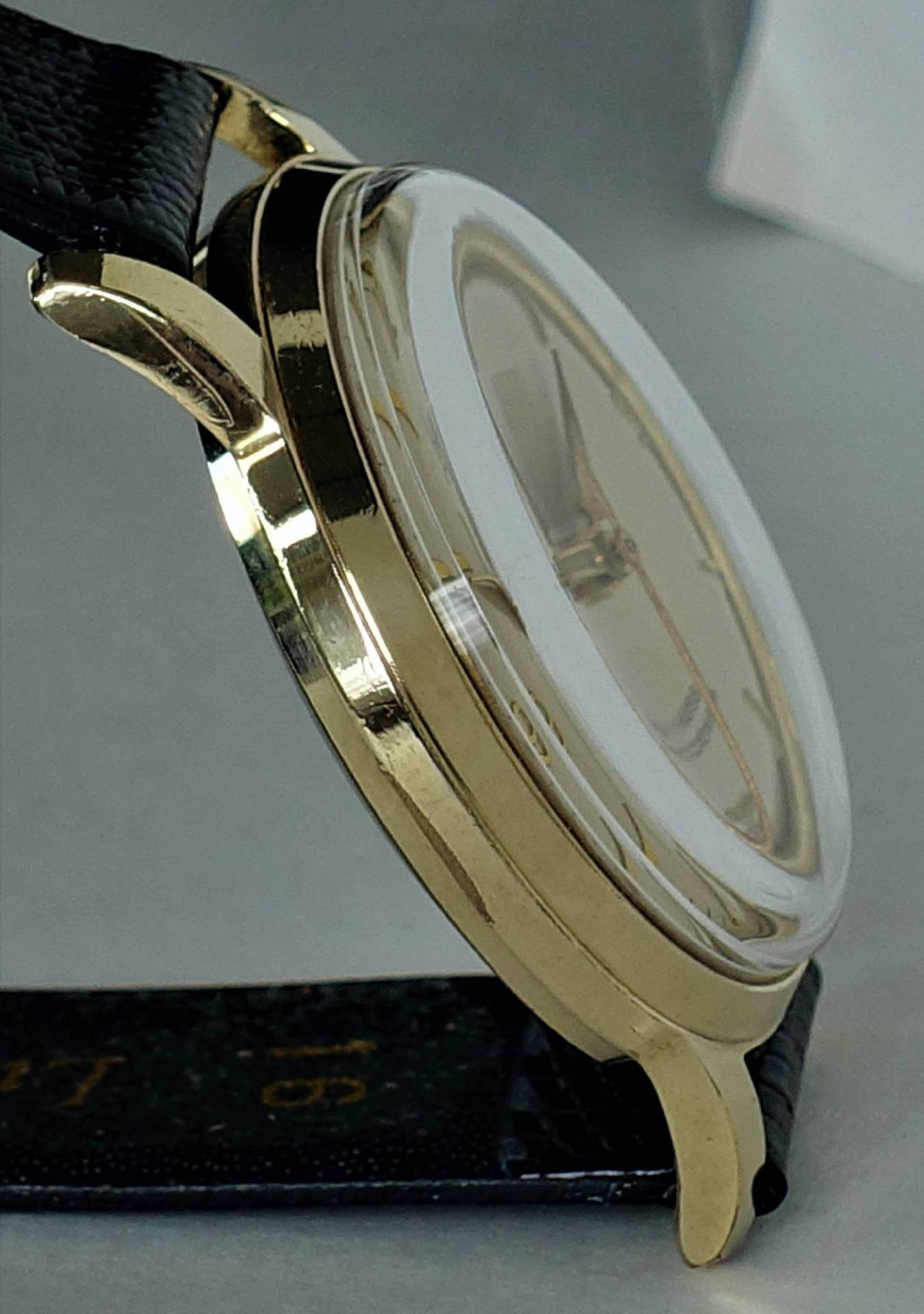 Flache Armbanduhr mit goldfarbenem Gehäuse und schwarzem Armband.