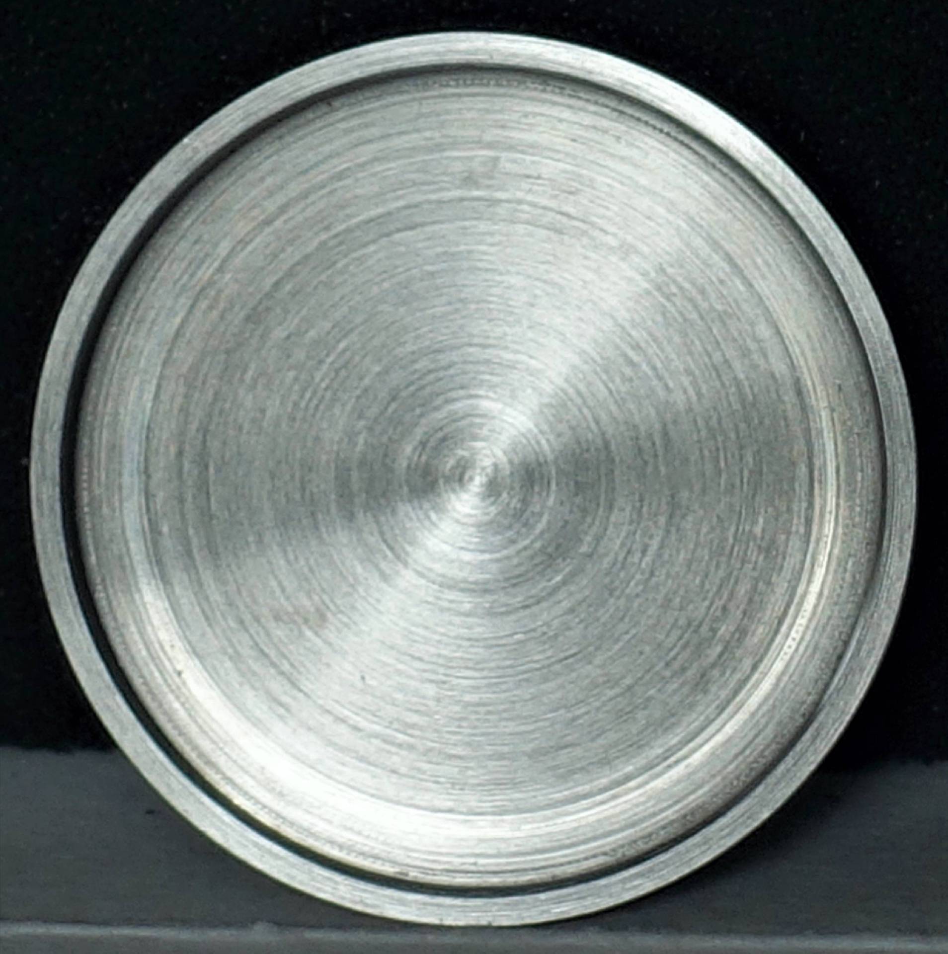 Runder Uhrenboden aus silberfarbenem Metall mit gebürsteter Oberfläche.