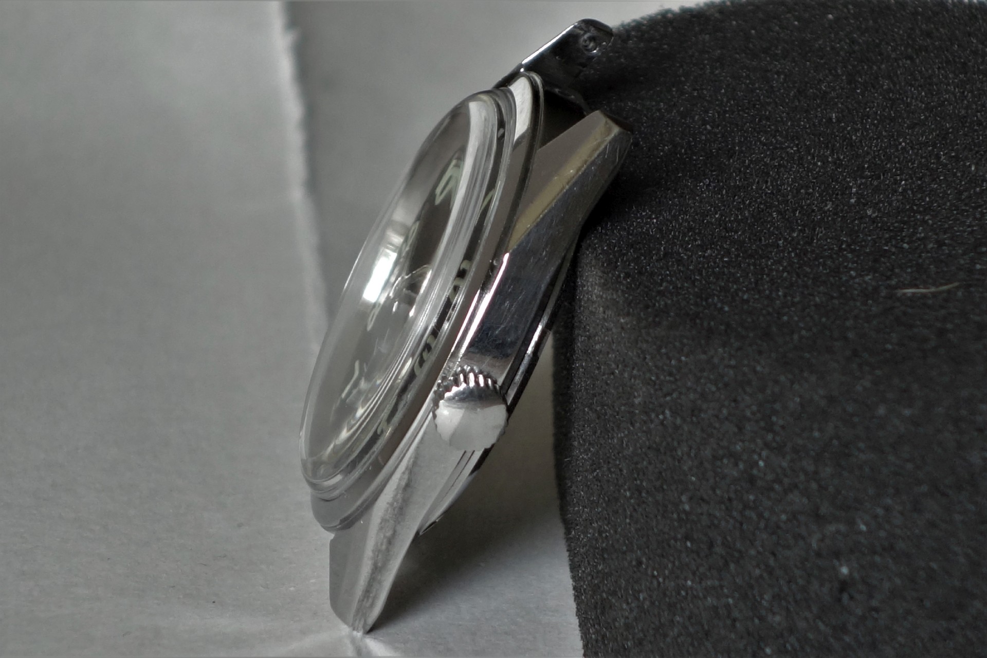 Silberfarbenes Uhrgehäuse mit Krone und Glas, seitliche Ansicht.