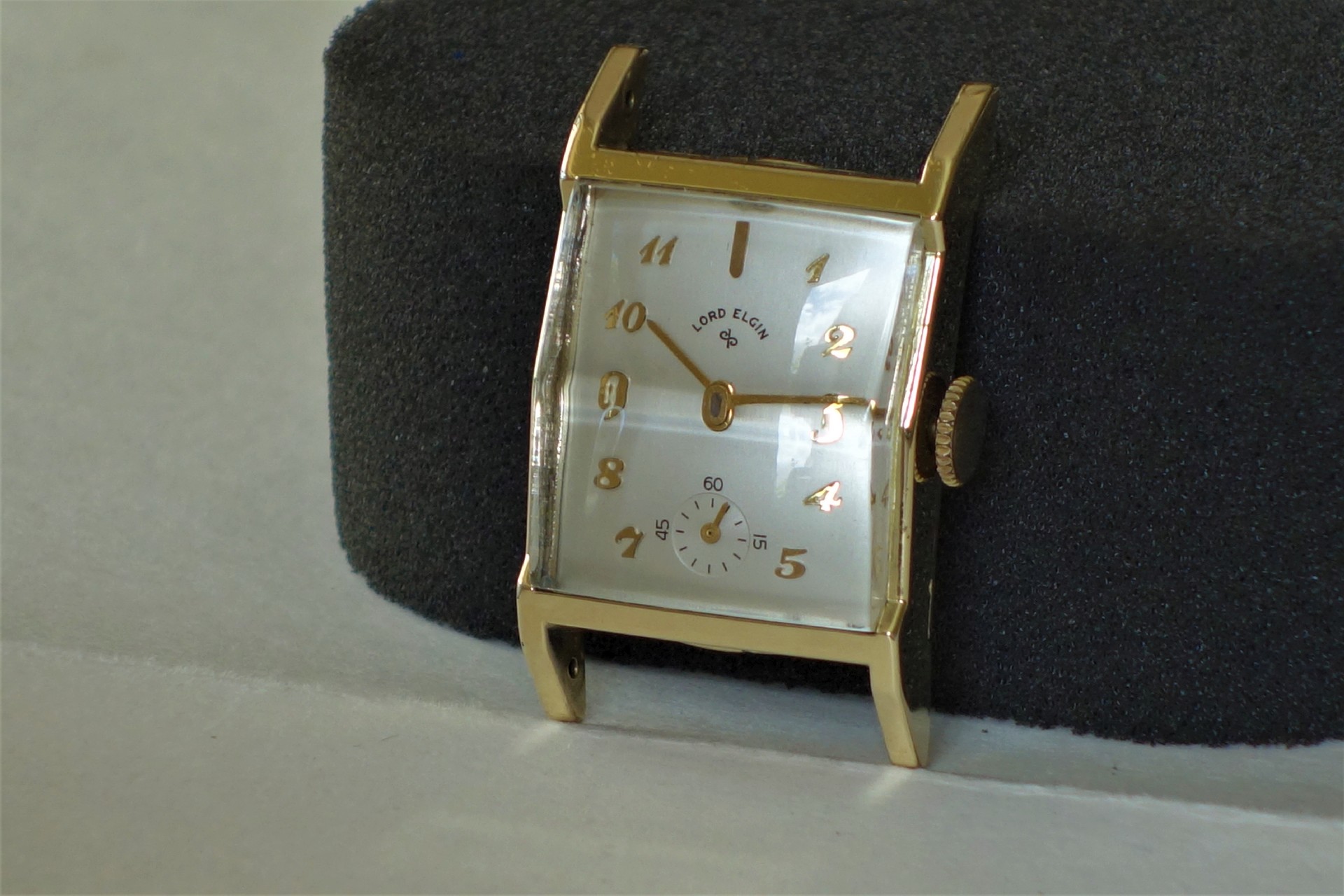 Rechteckiges goldfarbenes Uhrgehäuse mit Zifferblatt und Zeigern, ohne Armband.